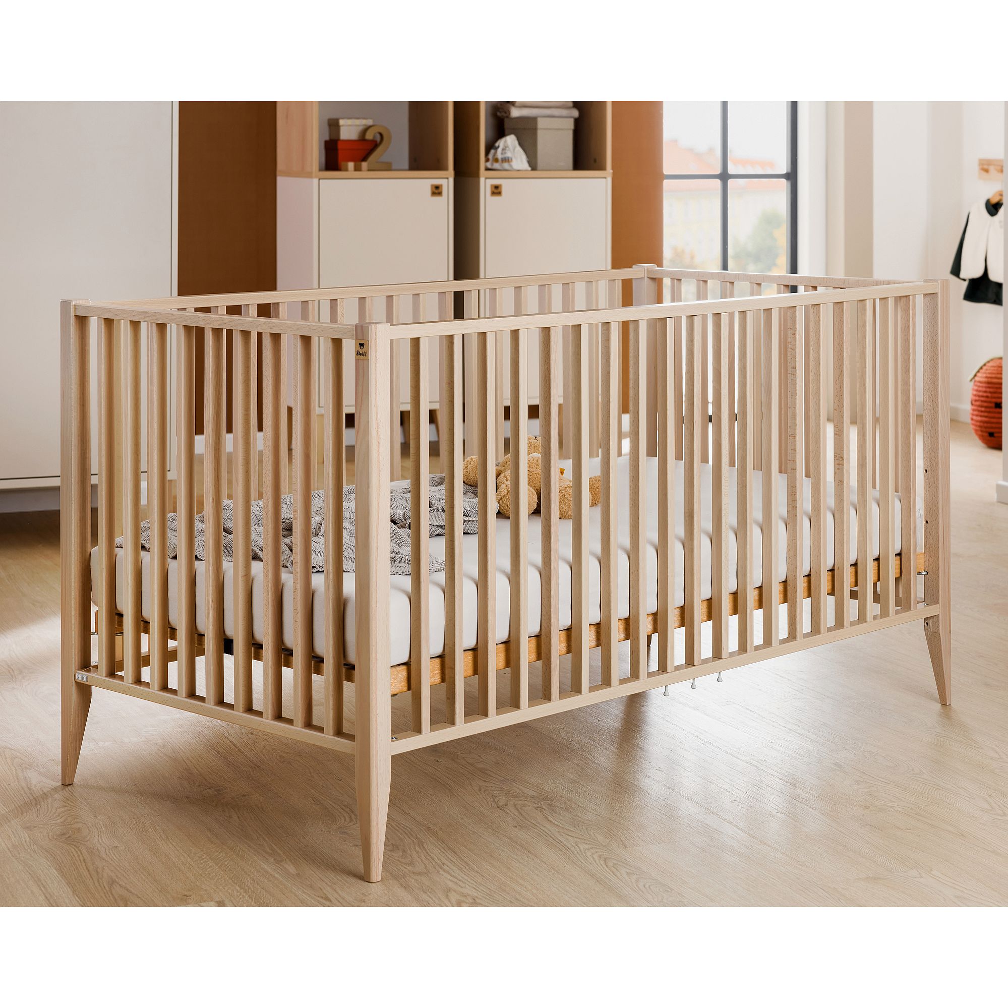 Ein Babybett aus Holz mit Lattenrost in einem modernen, hellen Kinderzimmer.