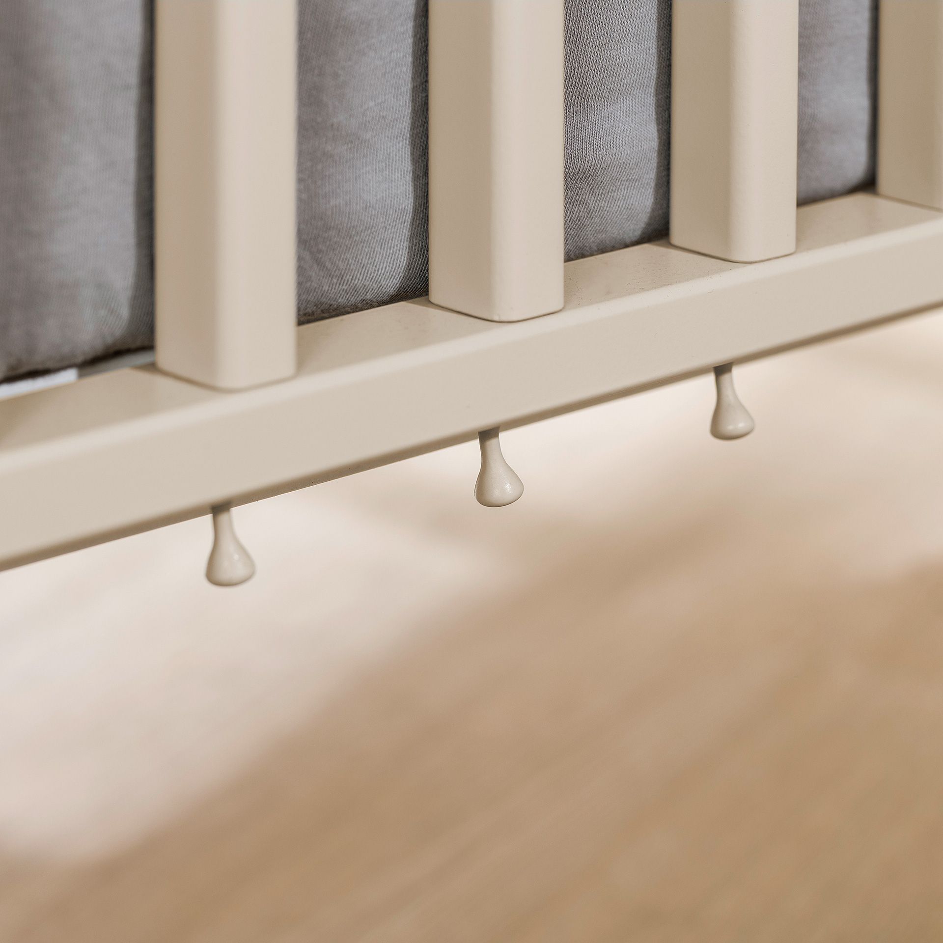 Nahaufnahme eines beigen Krippengitters mit tropfenförmigen Details darunter.