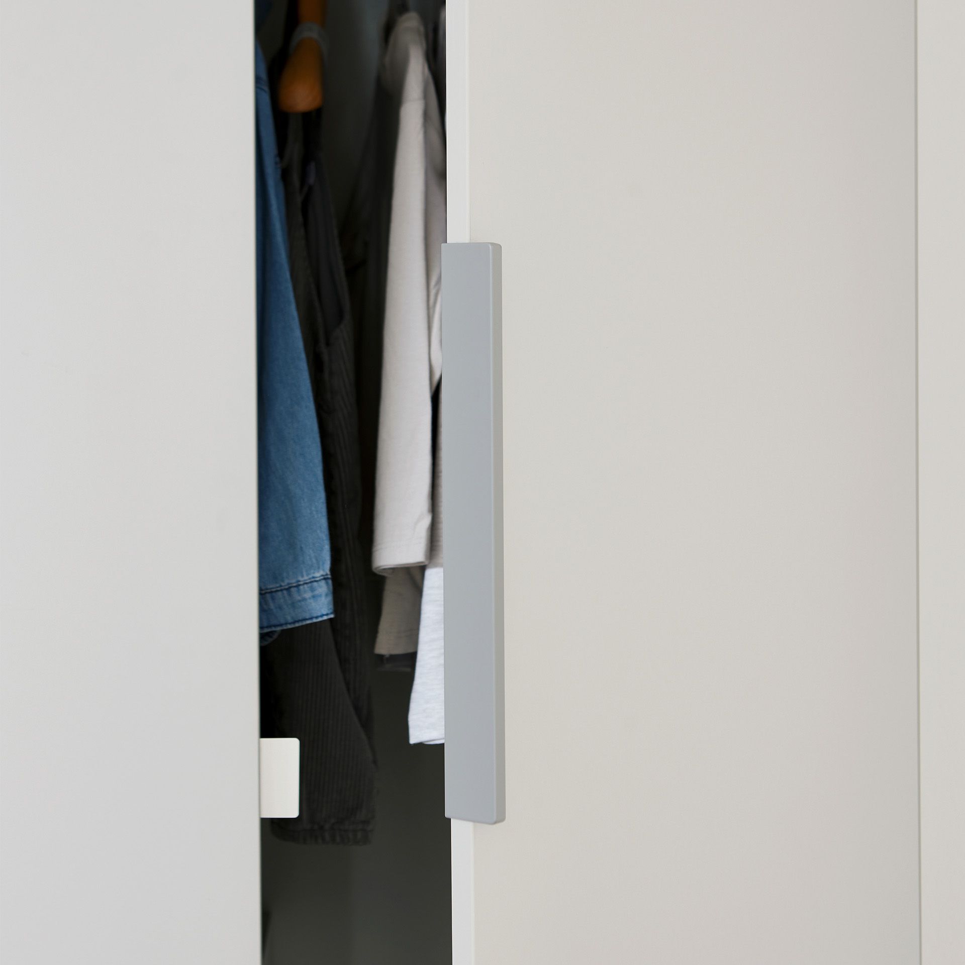 Drehtürenschrank Fiene mit 3 Türen und 1 Schublade Eine Schranktür ist leicht geöffnet und gibt den Blick auf hängende Kleidung frei.