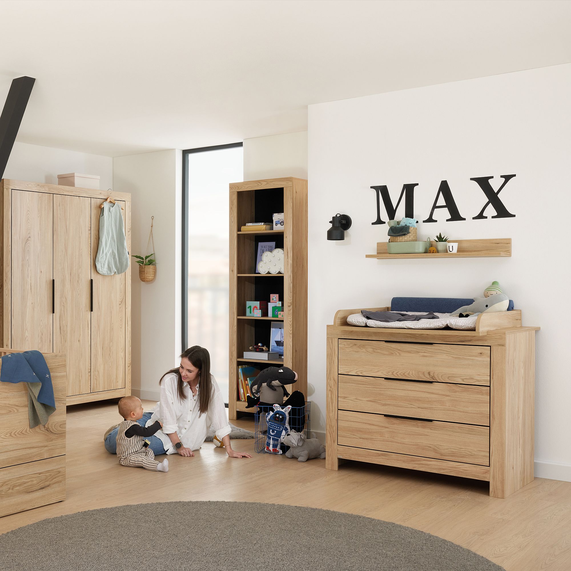 Frau und Baby spielen auf dem Boden in einem Kinderzimmer mit Holzmöbeln und Spielzeug.