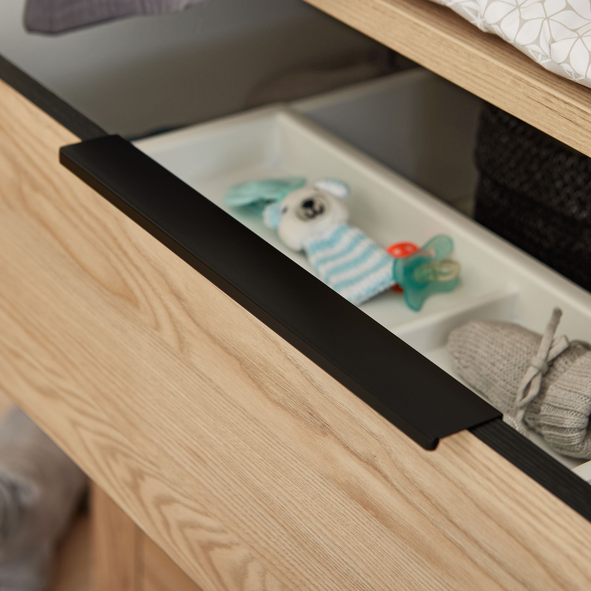 Öffnen Sie eine Holzschublade mit einem Kuscheltier, Schnullern und Babyfäustlingen darin.