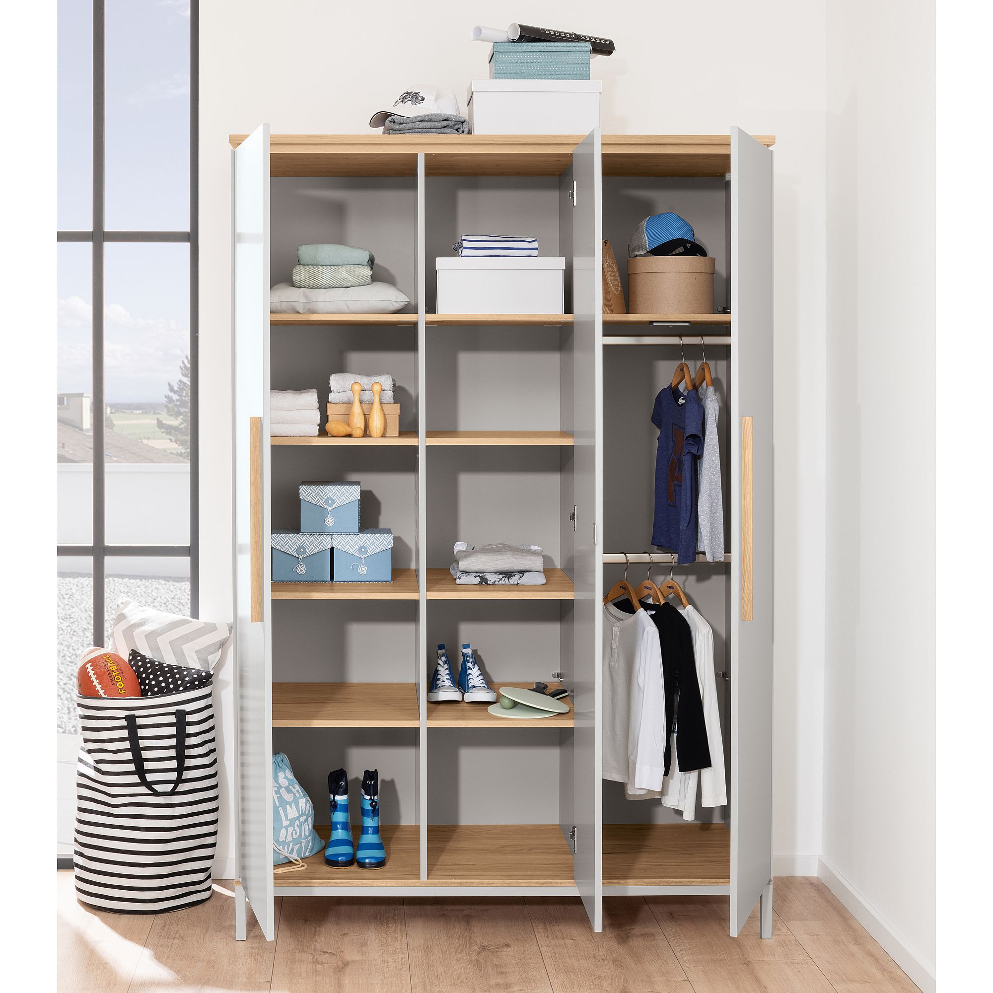 Offener Kleiderschrank mit Regalen, Kleidern, Schuhen, Kisten und Körben darin.