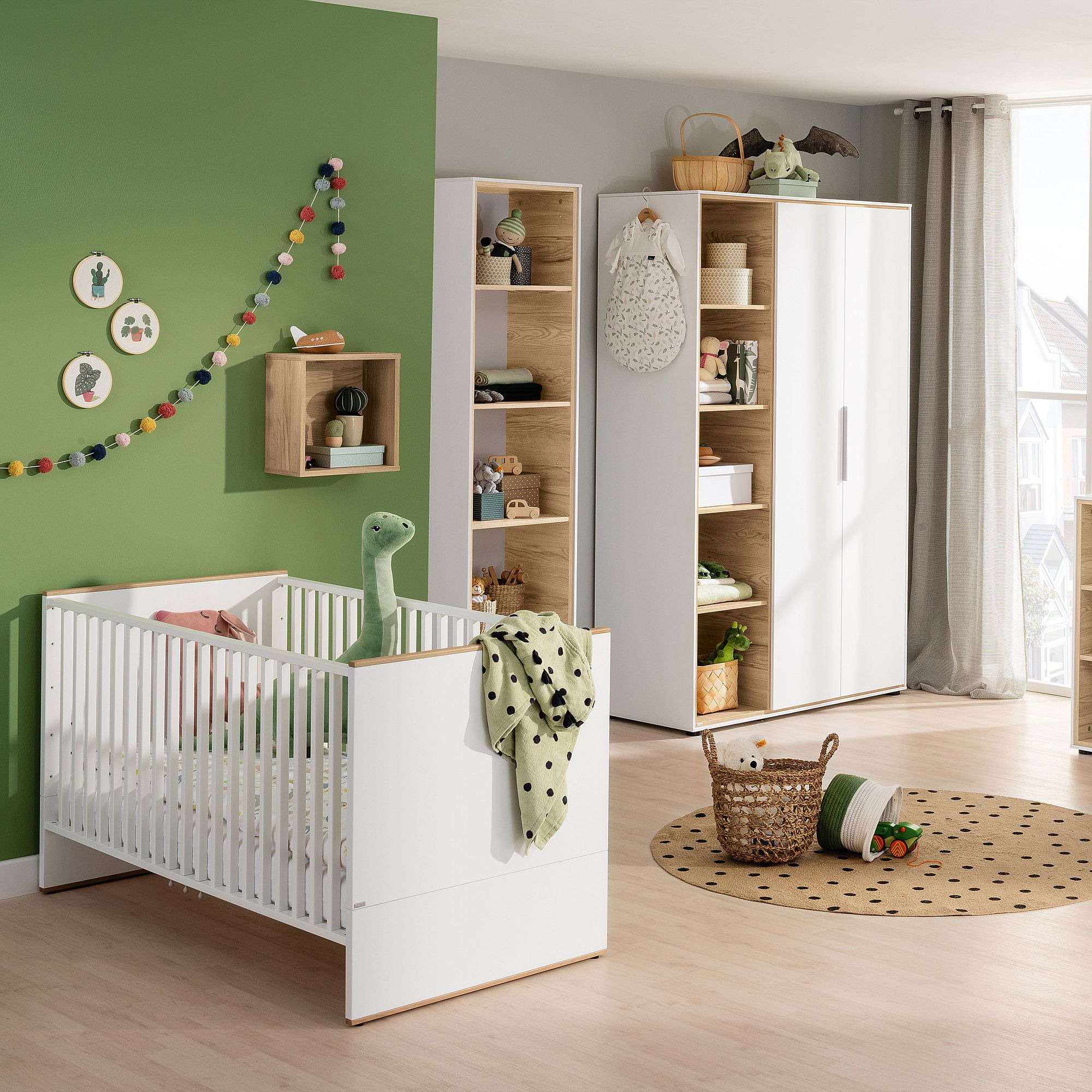 Modernes Kinderzimmer mit einem weißen Kinderbett, grünen Akzenten und Aufbewahrungsmöbeln aus Holz.