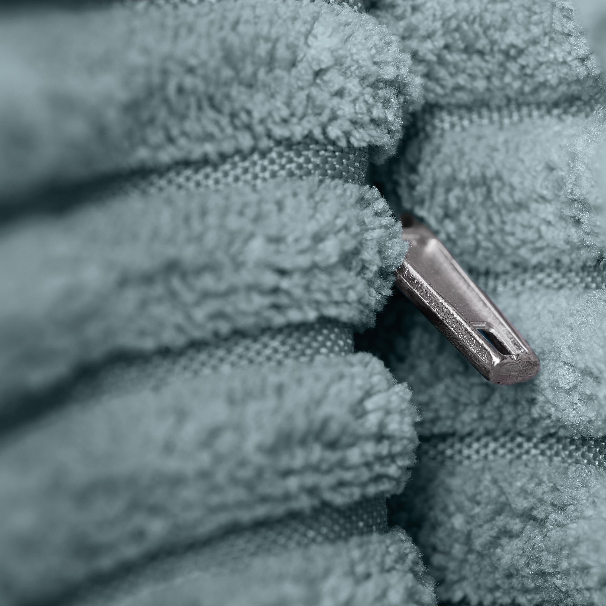 Nahaufnahme eines silbernen Reißverschlusses, der teilweise zwischen weichem, flauschigem blauem Stoff verborgen ist.