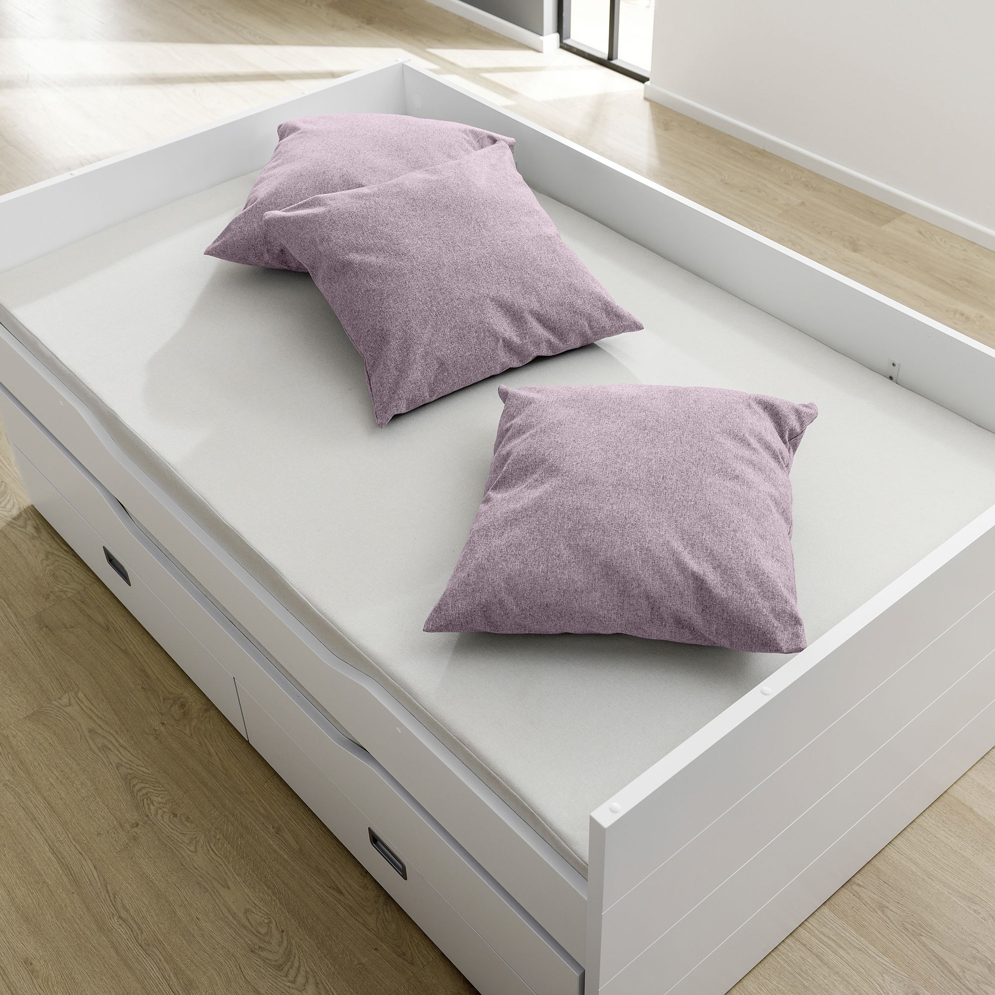A white bed with two purple pillows on a light mattress in a bright room.
