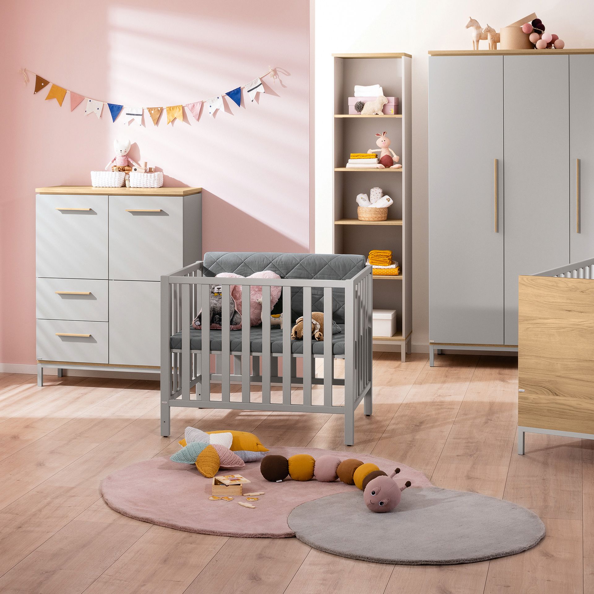 Modern nursery with a gray crib, toys, pastel decor, and wooden furniture.