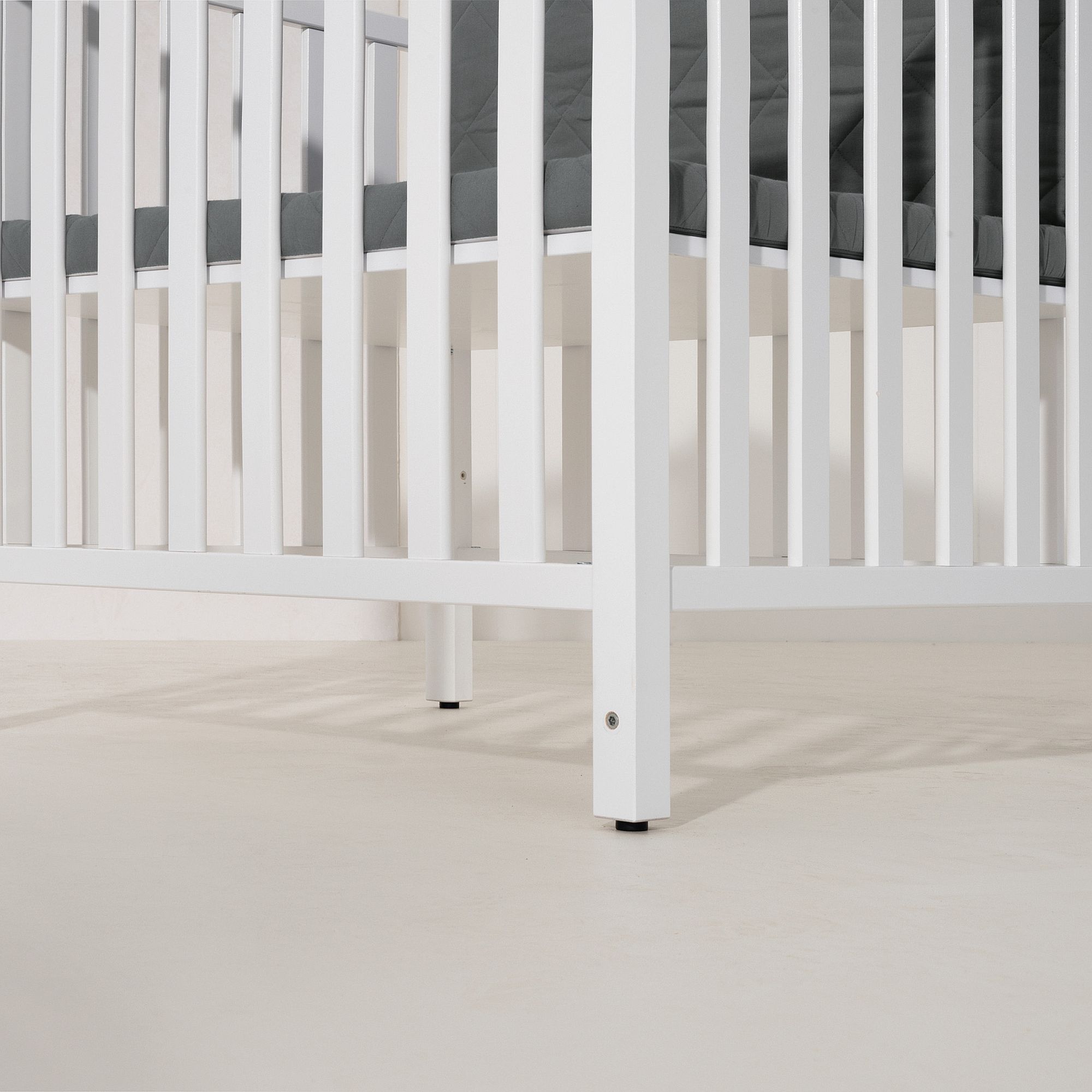 White wooden crib with a dark mattress on a light-colored floor.