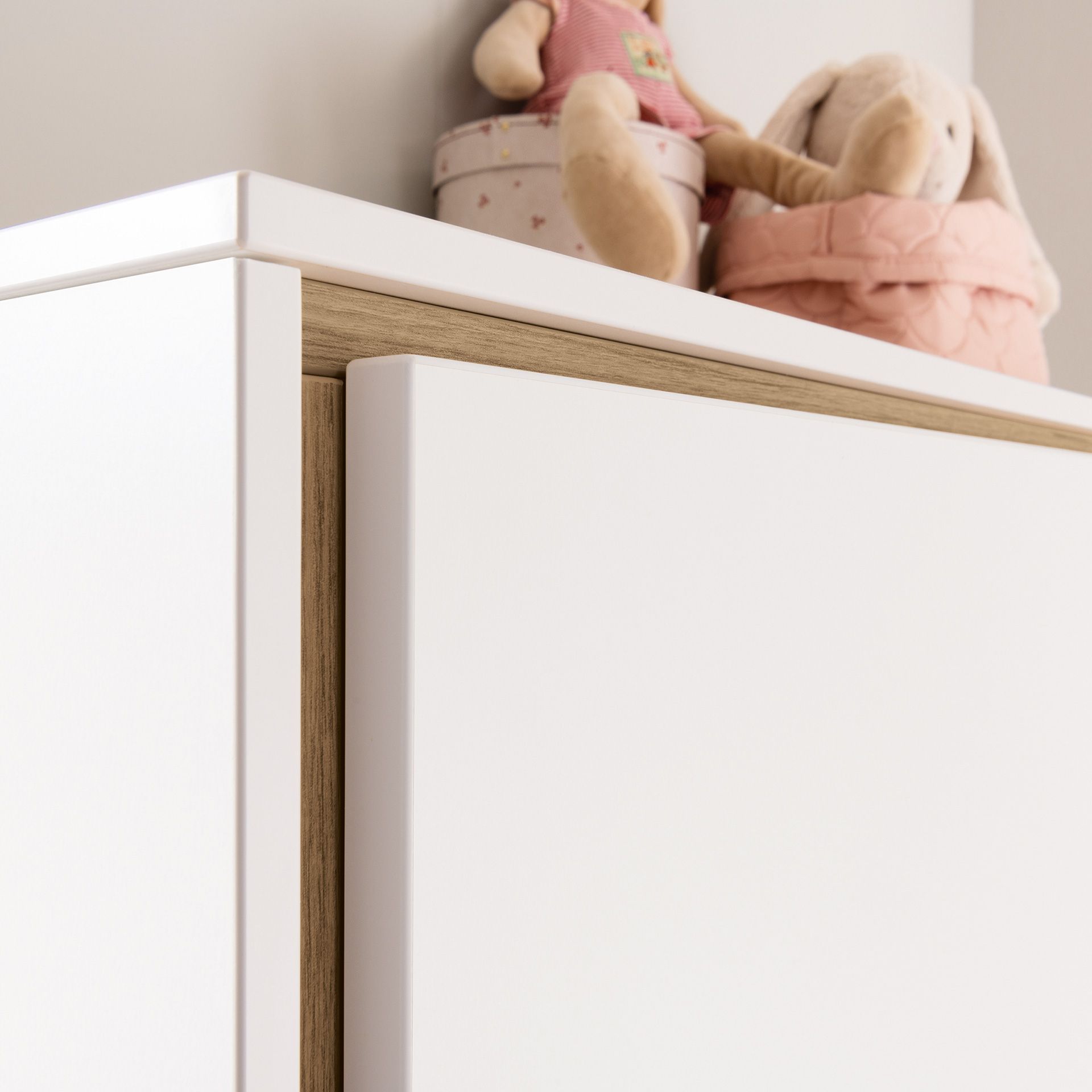 Auf einem weißen Schrank stehen zwei Stofftiere und eine runde Schachtel.