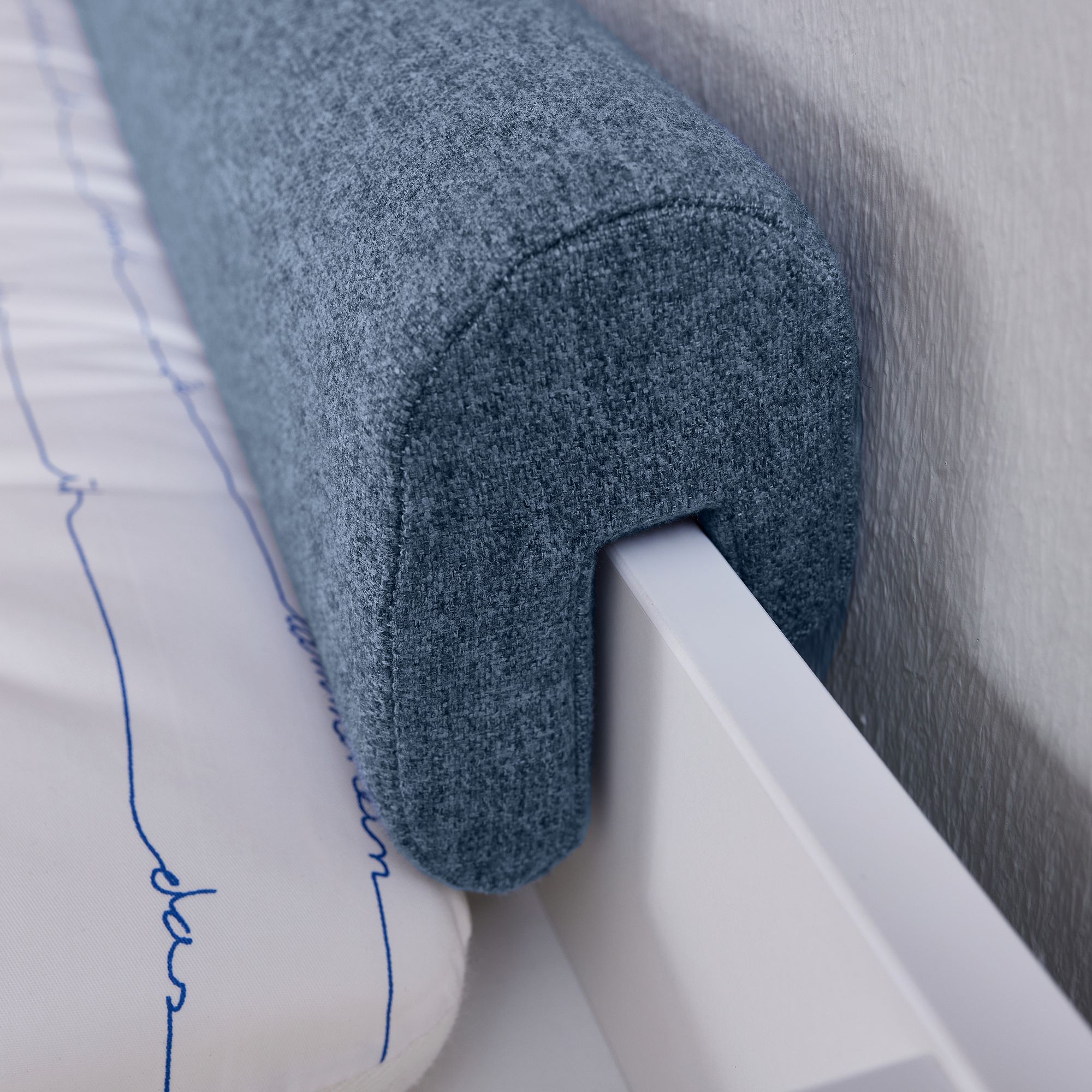 Blue upholstered bed bumper attached to the side rail of a white bed frame.