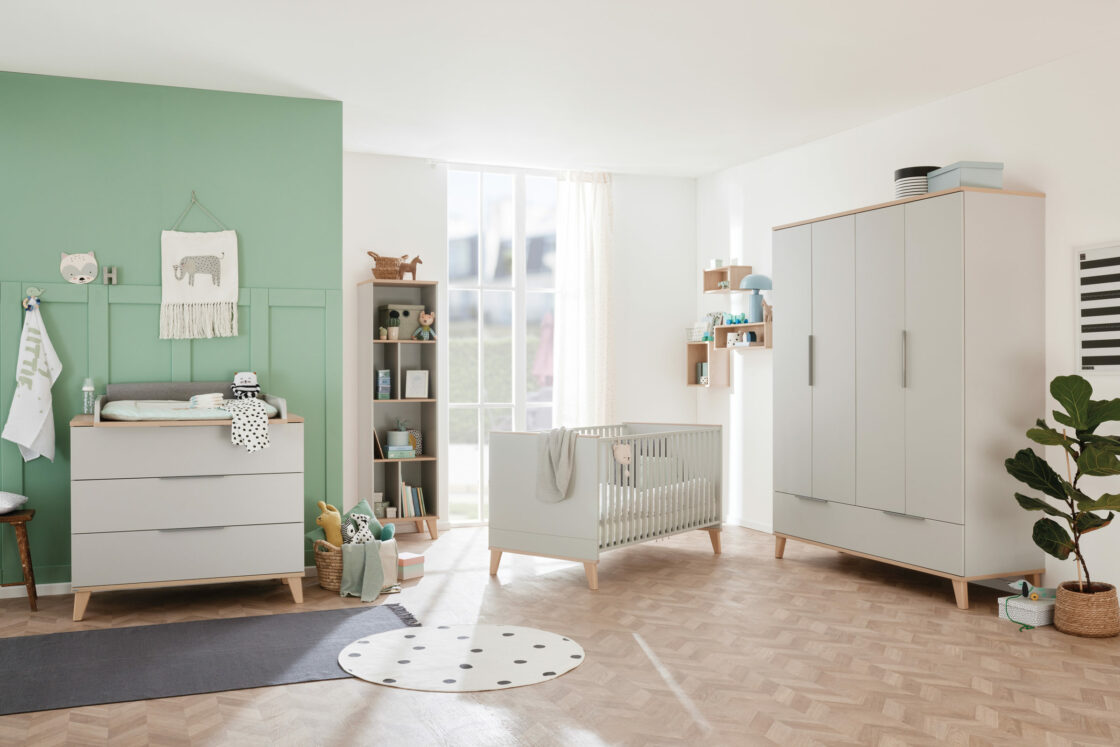 Modern nursery with mint green accent wall, crib, dresser with changing pad, wardrobe, toys, and natural light from large window.