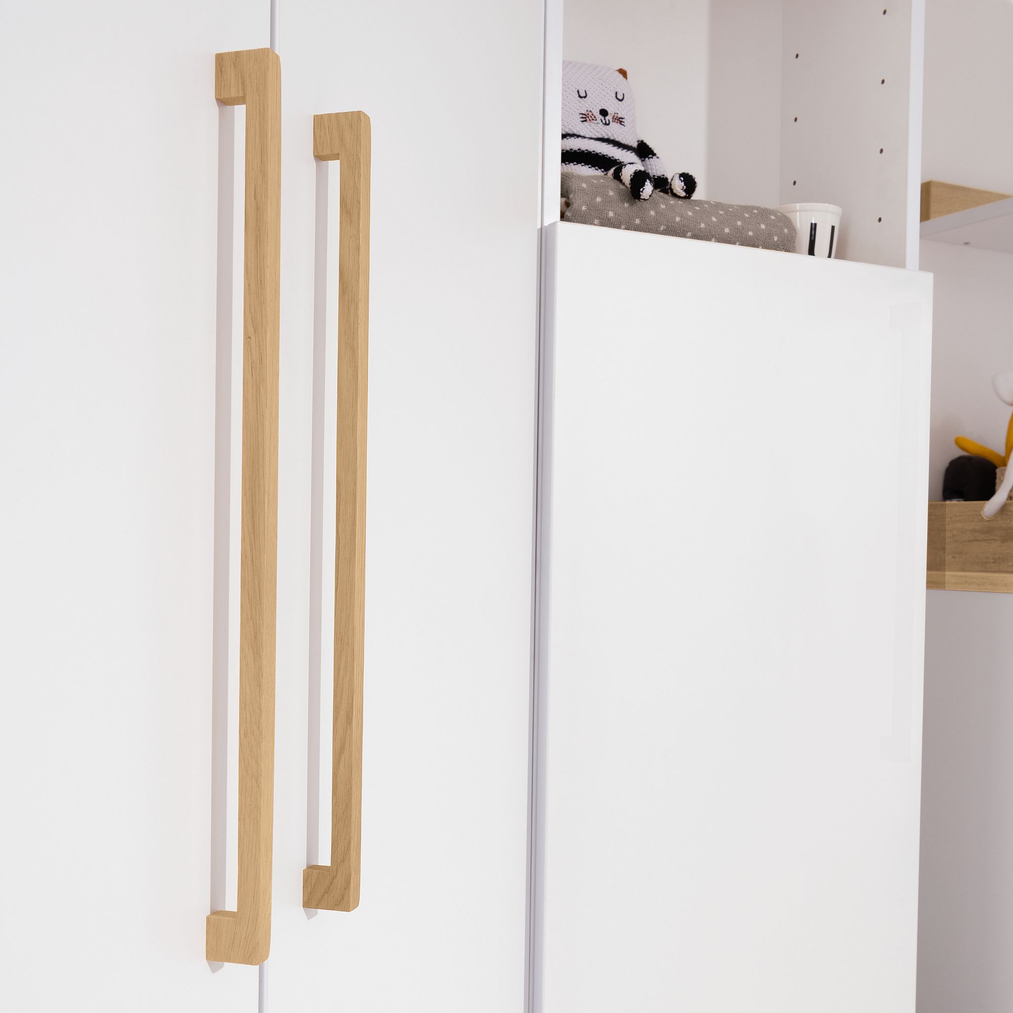 Weiße Schränke mit Holzgriffen und einem Stofftier auf dem obersten Regal.