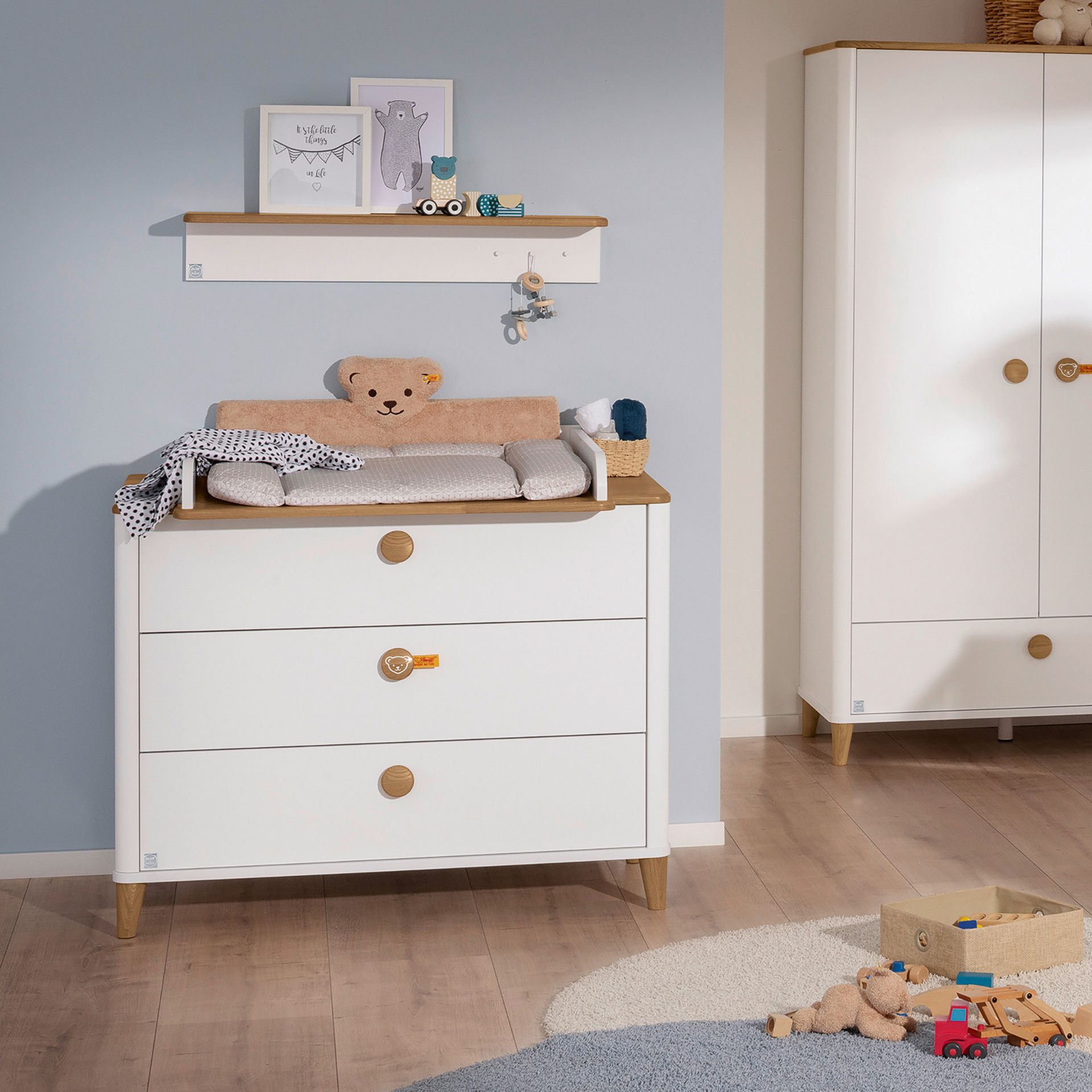 Modern nursery with a changing table, teddy bear, toys, and pastel decor.