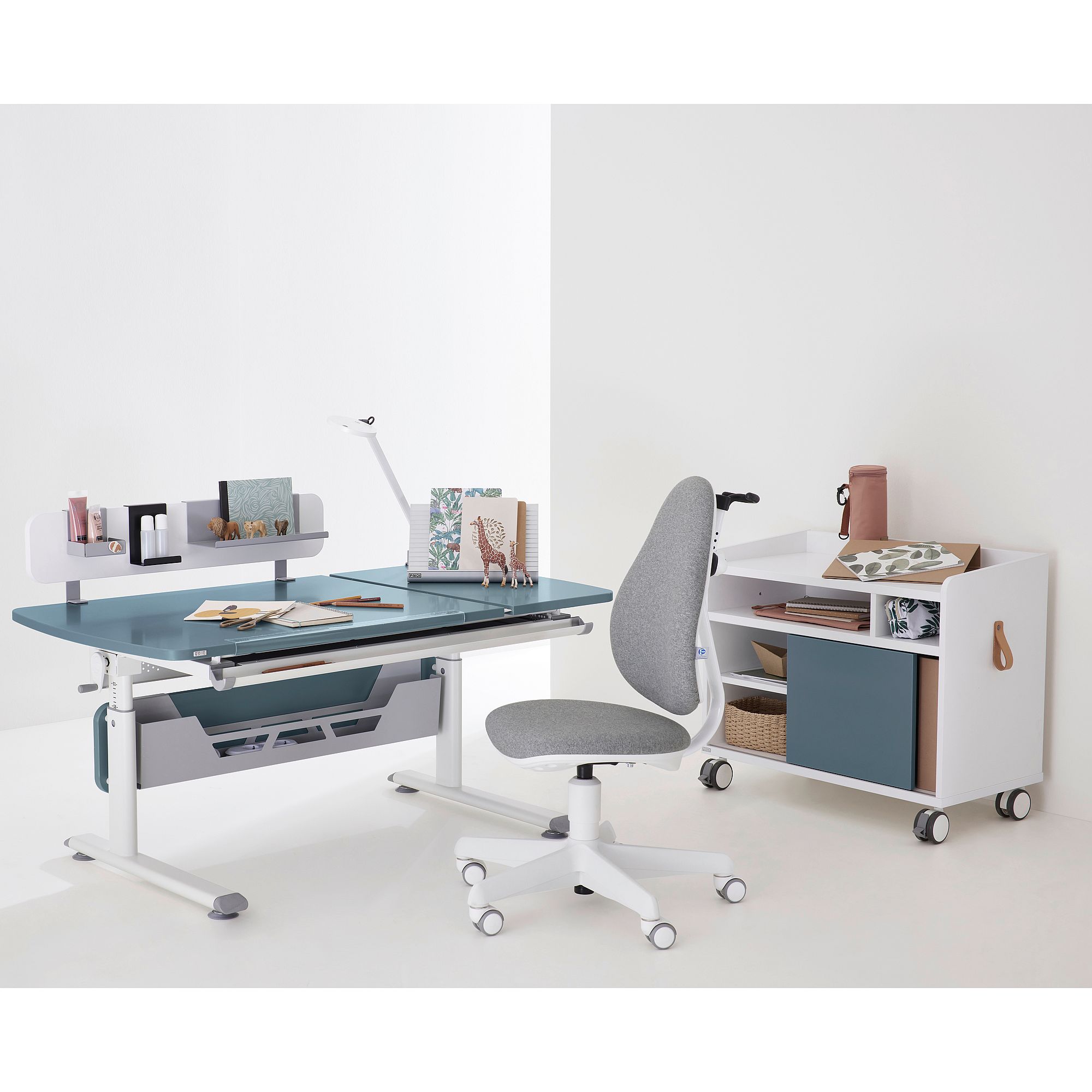 Schülerschreibtisch Diego GT Curved mit geteilter Platte 130 x 70 cm in Mattblau Moderner Arbeitstisch mit grauem Stuhl und Aufbewahrungswagen in einem minimalistischen weißen Raum.