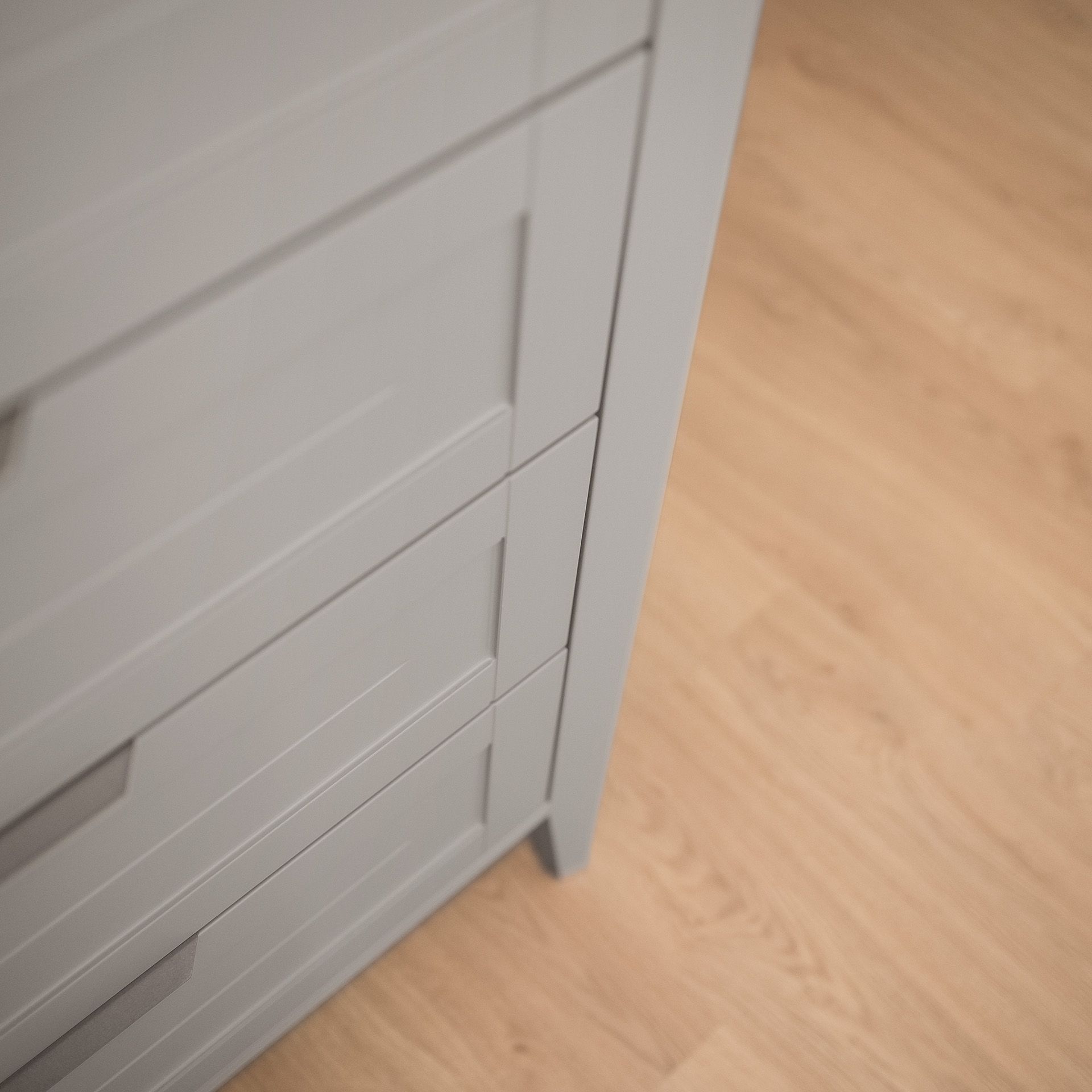 Close-up of a light gray dresser next to a light wood floor.