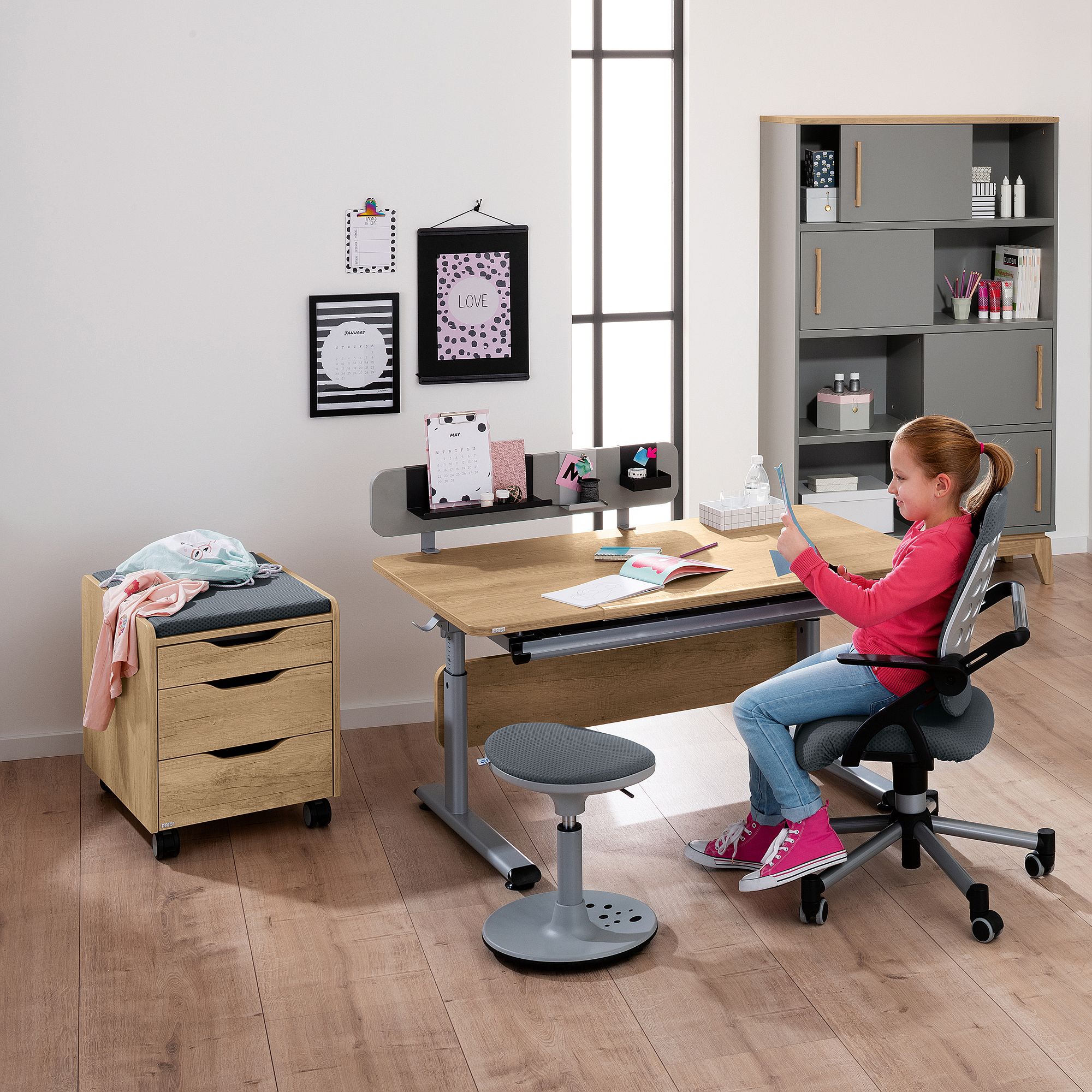Ein junges Mädchen sitzt an einem Schreibtisch in einem modernen, aufgeräumten Arbeitszimmer und benutzt ein Tablet.