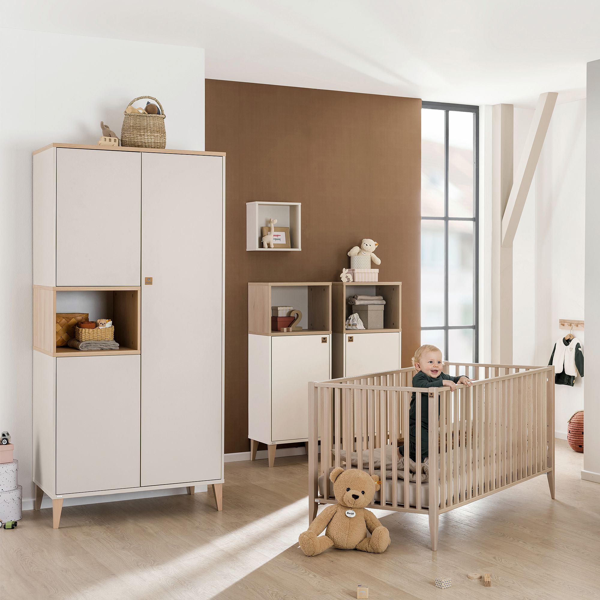 Ein Baby steht in einem Holzbettchen in einem modernen, lichtdurchfluteten Kinderzimmer.