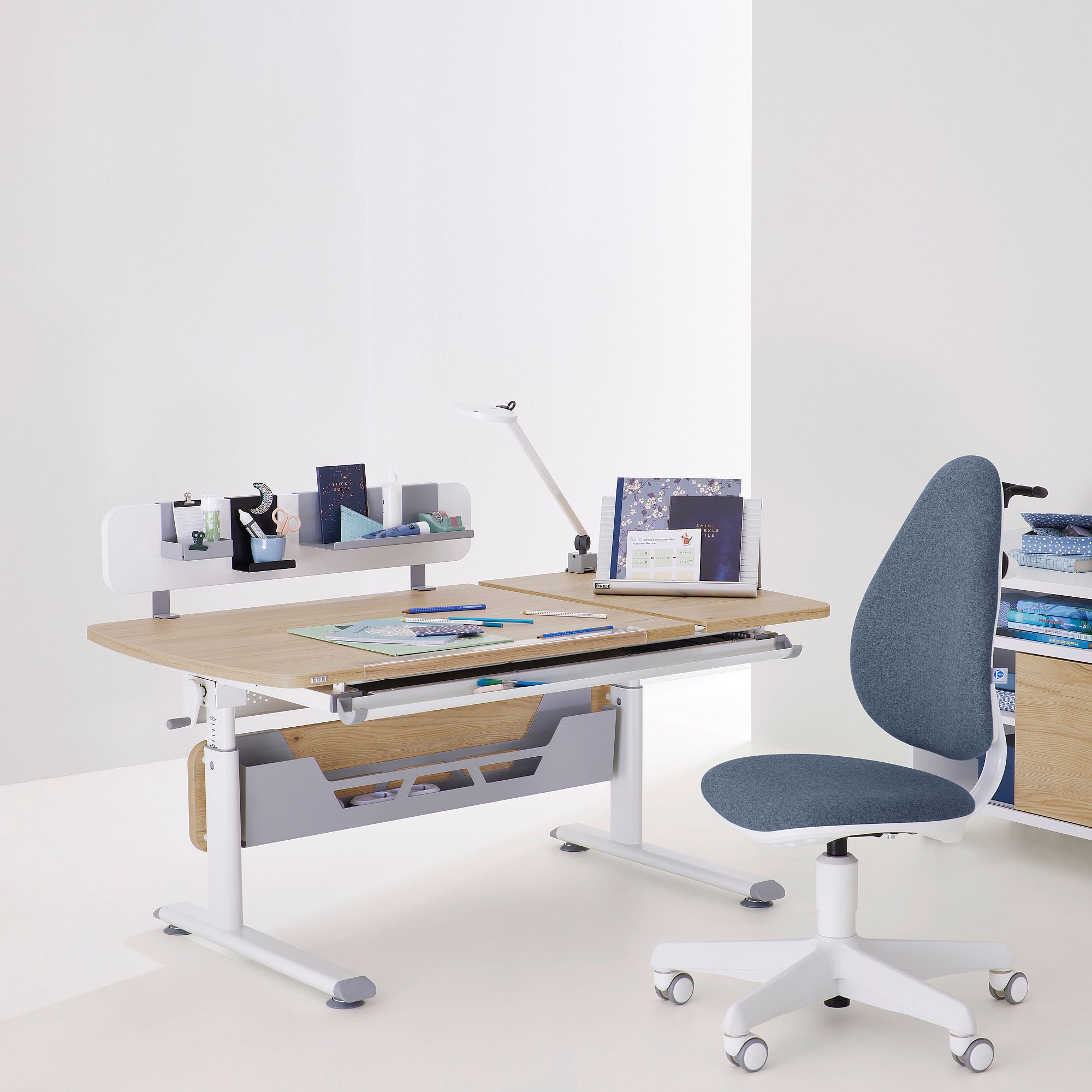 Moderner Arbeitstisch mit Büchern, Lampe und grauem Bürostuhl in einem hellen Raum.