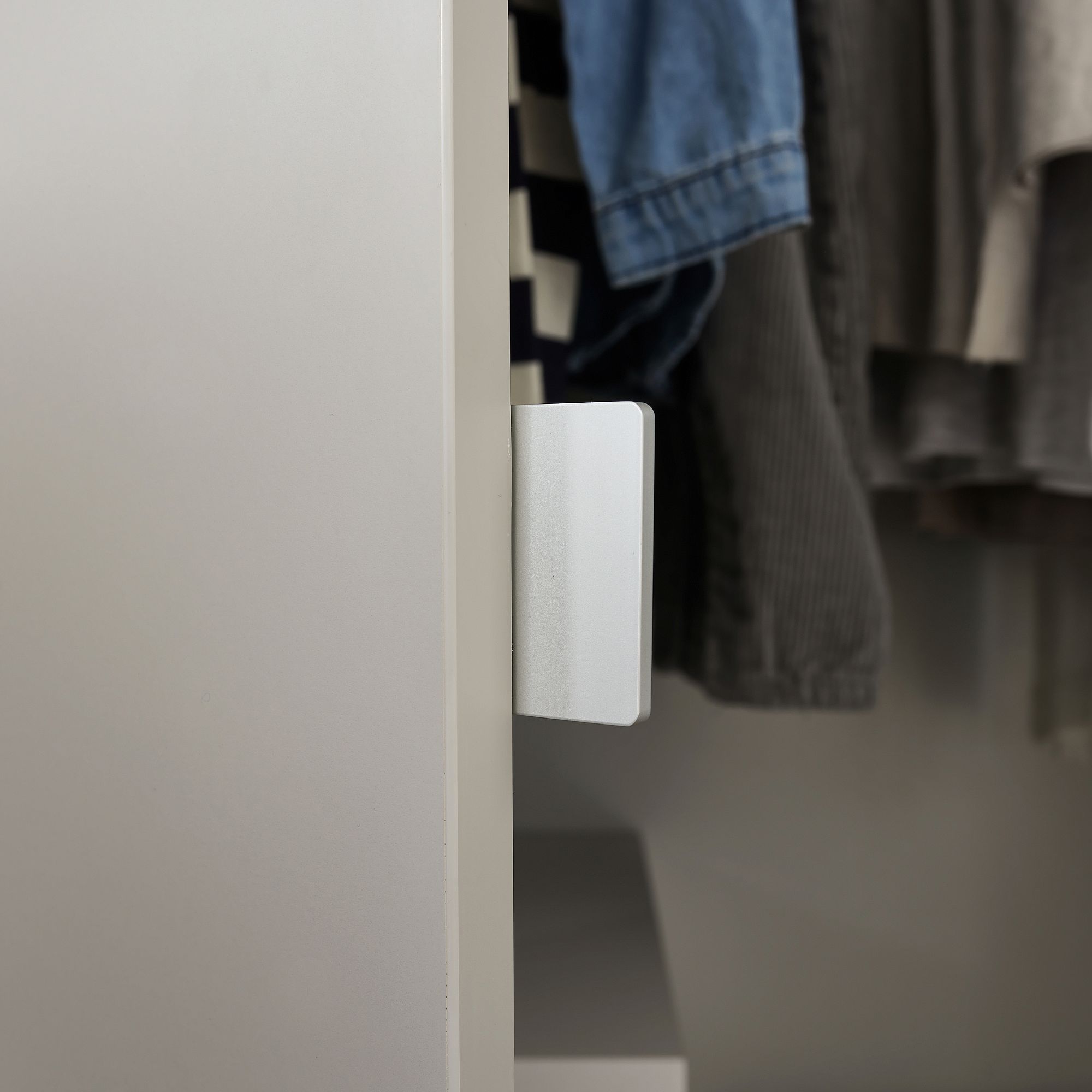 Ein weißer Sensor wird an der Kante einer Schranktür angebracht, in der sich Kleidung befindet.