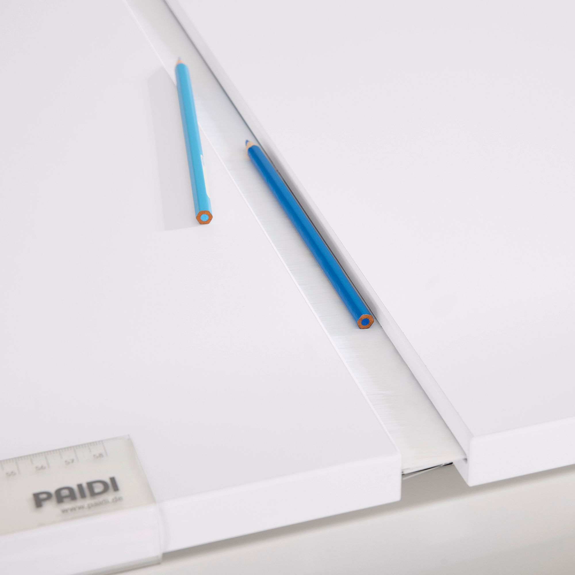 Schülerschreibtisch Diego GT Curved mit geteilter Platte 130 x 70 cm in Kreideweiß Zwei blaue Bleistifte und ein Lineal auf einer weißen Fläche mit einem schmalen Spalt.