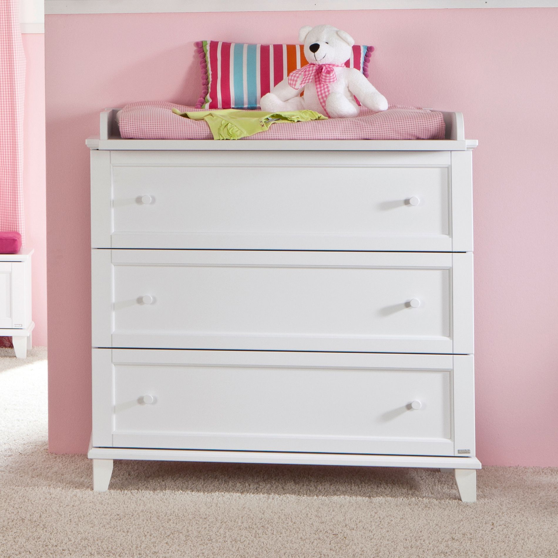 White dresser with three drawers, striped pillow, and a teddy bear on top.