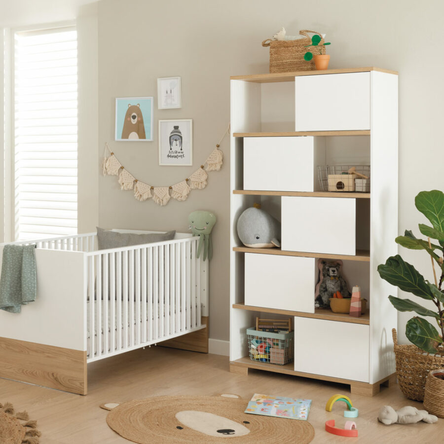 Bright, modern nursery with a white crib, toys, books, and a tall white shelving unit beside a potted plant and animal decor.
