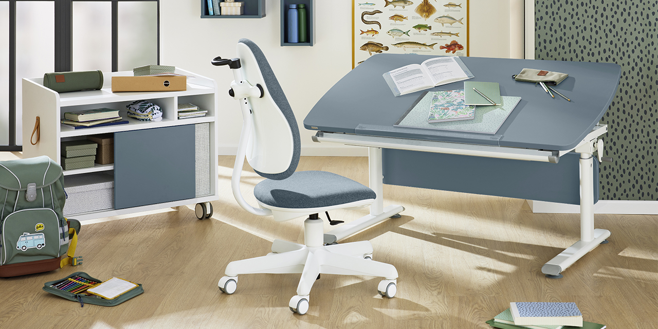 1106_PAIDI_Shop_Programme_DiegoCurved_Header-ID1692496_1a0f1527-5a3e-7b9d-1924-16e2090a7f38.jpg Modernes Arbeitszimmer mit blauem verstellbarem Schreibtisch, ergonomischem Stuhl, Regalen, Büchern, Landkarte, Rucksack und Fischposter an der Wand.