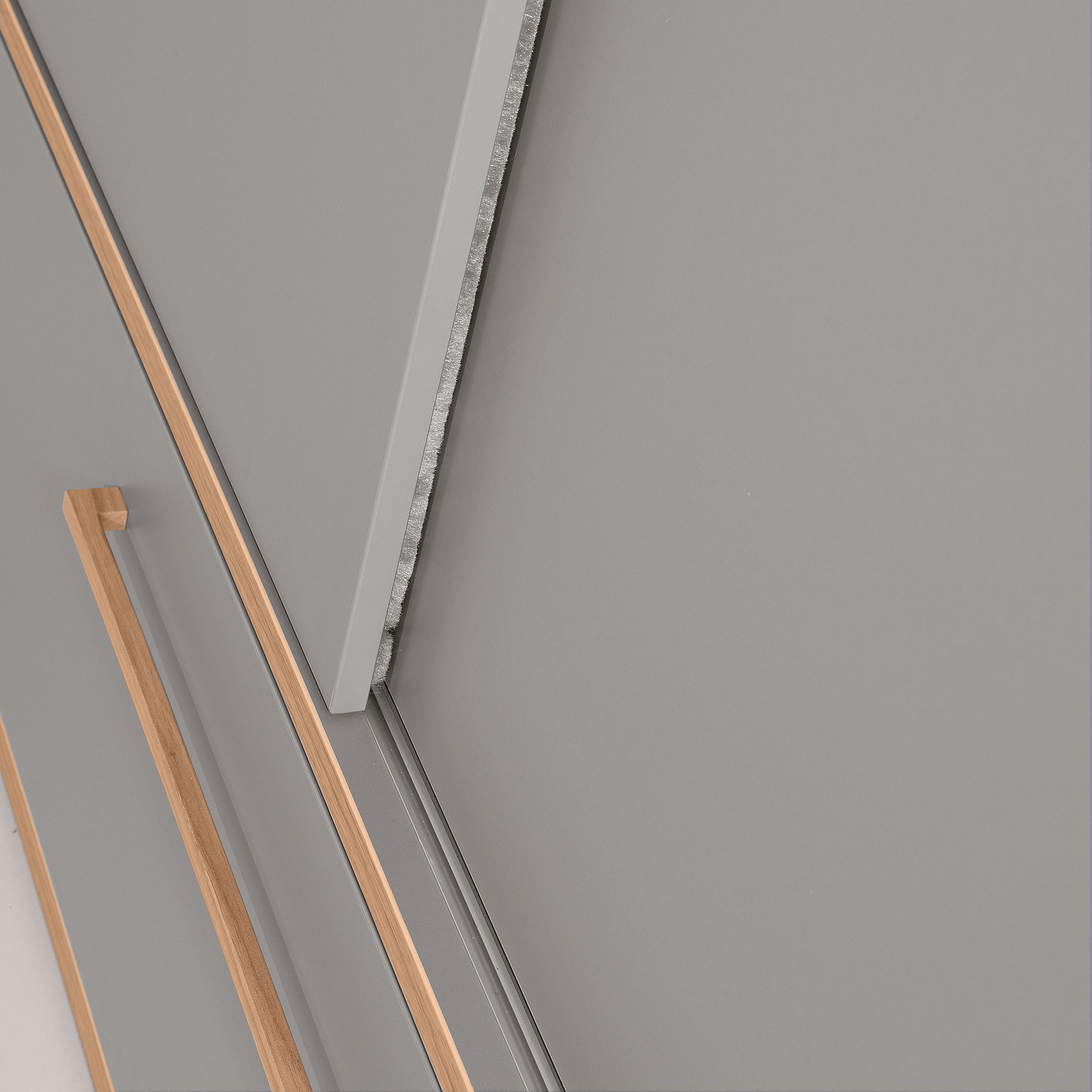 Nahaufnahme moderner grauer Schranktüren mit Holzgriffen und abgeschrägtem Design.