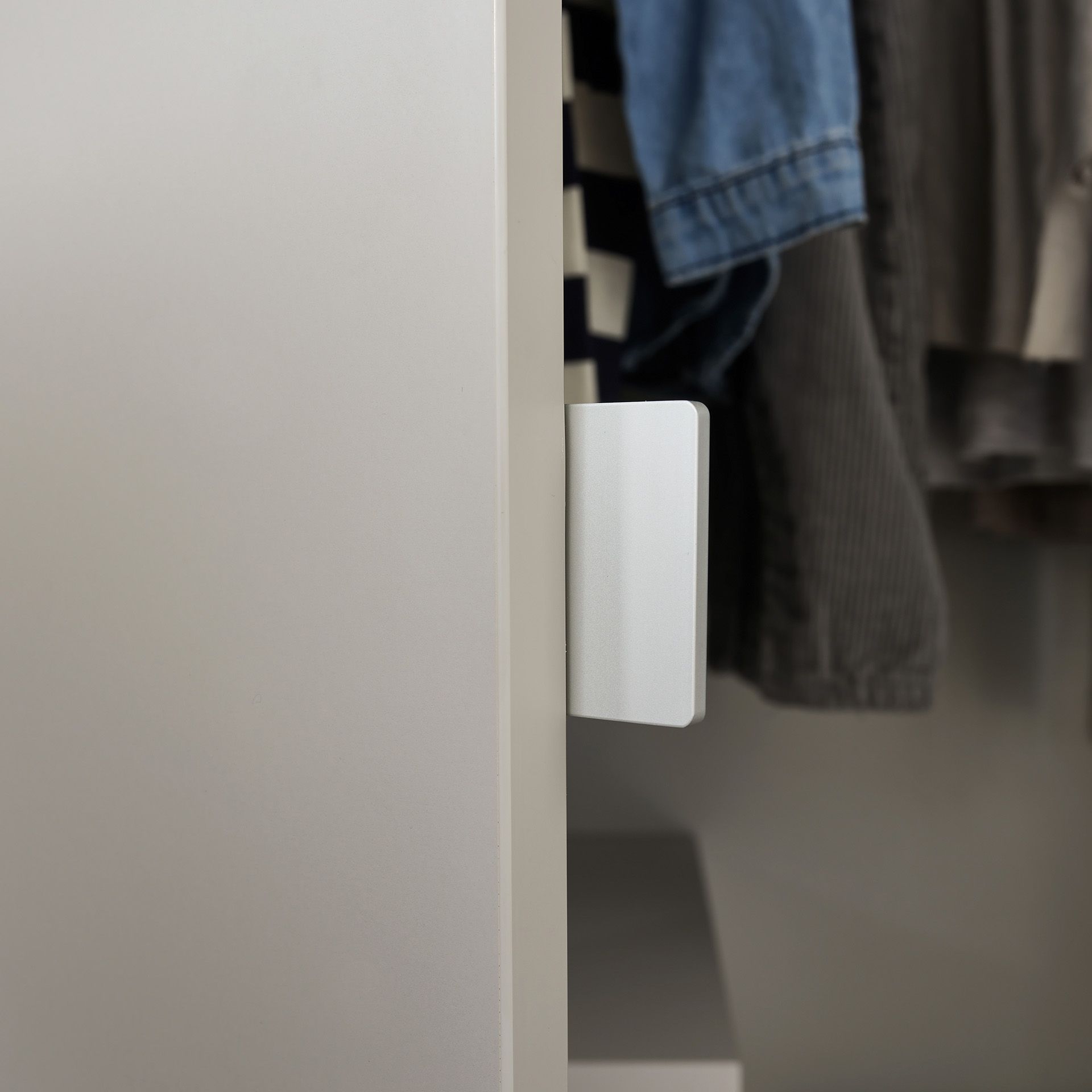 Drehtürenschrank Fiene mit 3 Türen und 1 Schublade Weiße, leicht geöffnete Schranktür, in der Kleidung hängt.