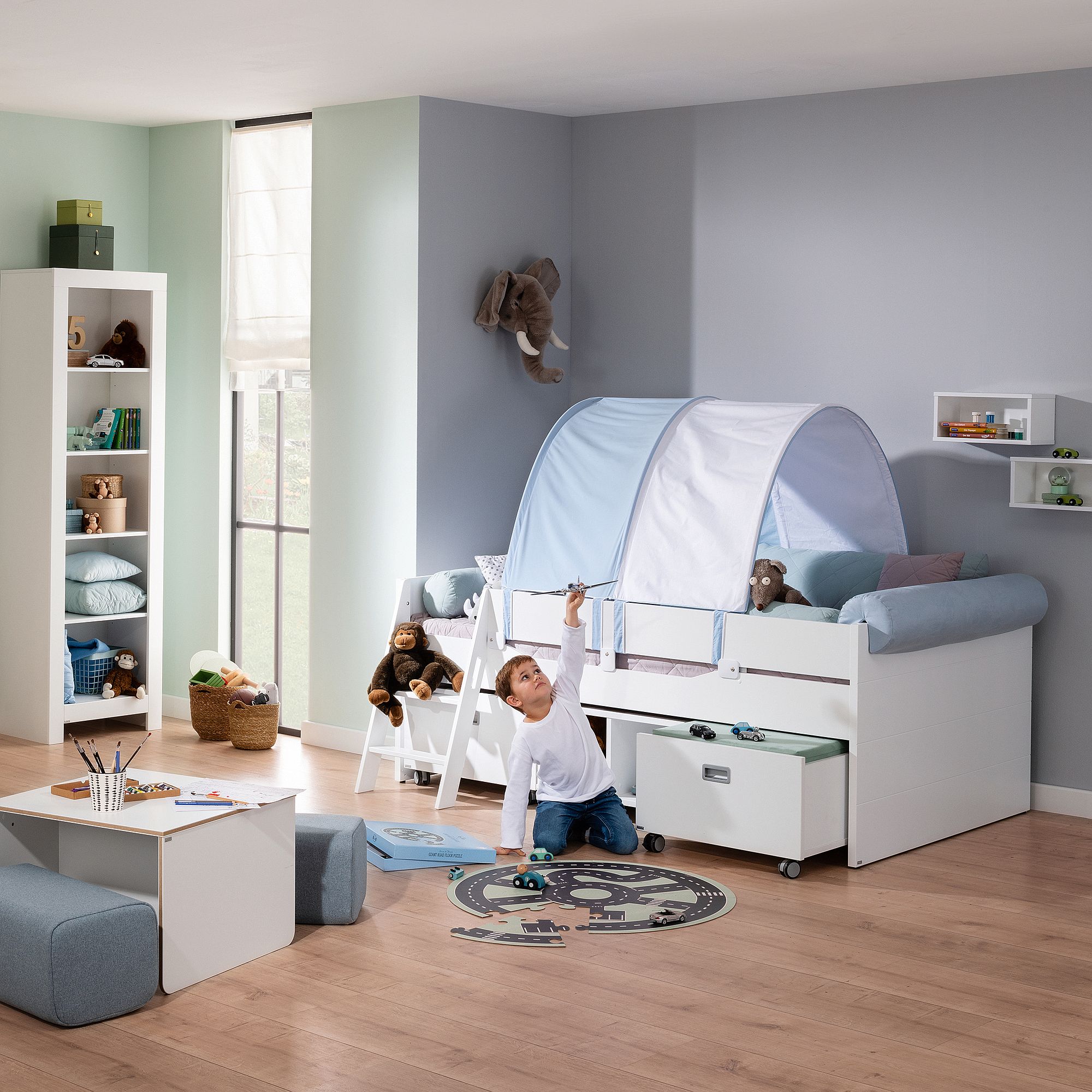 Ein Kind spielt mit einem Spielzeugflugzeug in einem ordentlich eingerichteten Schlafzimmer mit einem Bett, das wie ein Zelt aussieht.