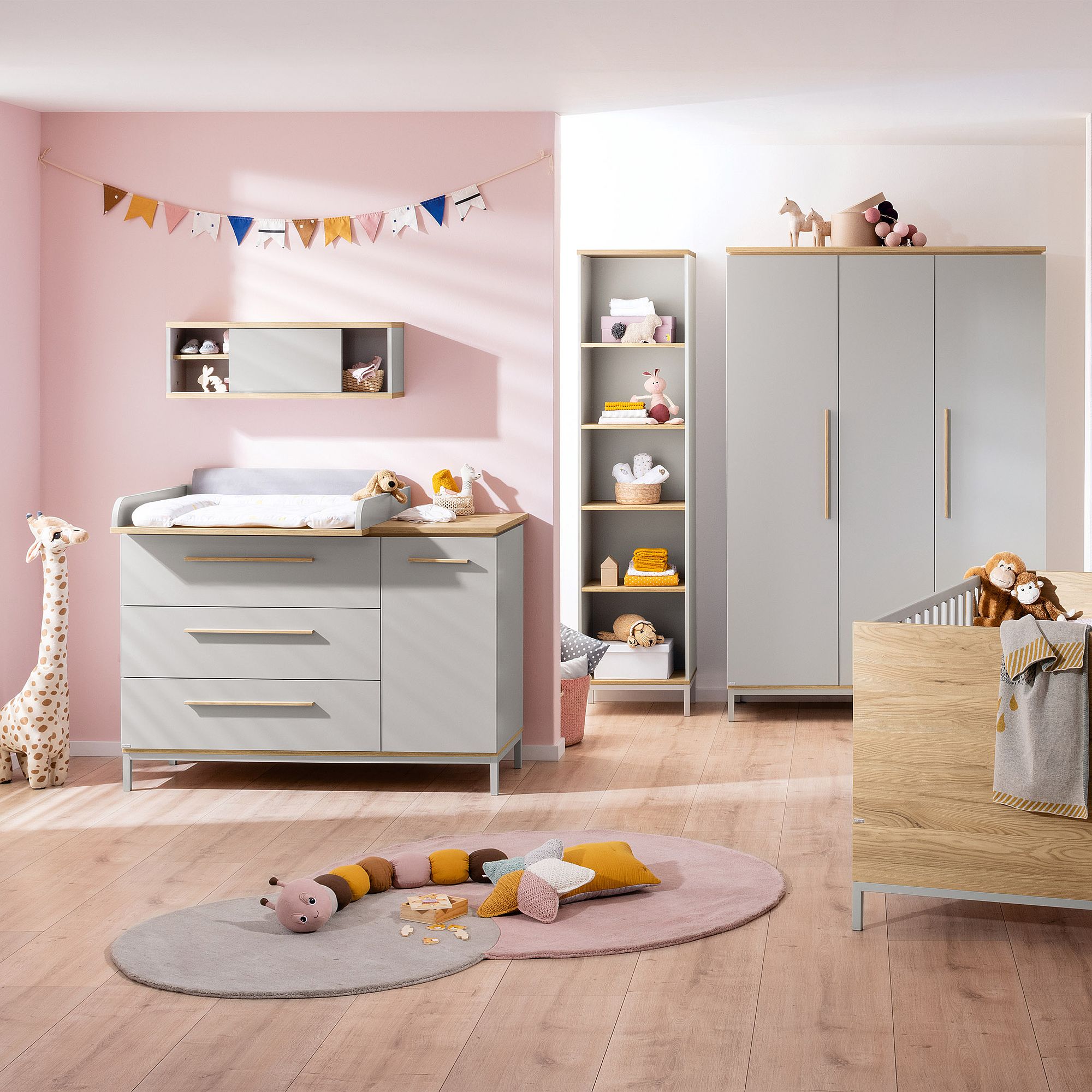 Modernes Kinderzimmer mit rosa Wänden, grauen Möbeln, Spielzeug und dekorativen Wimpeln.
