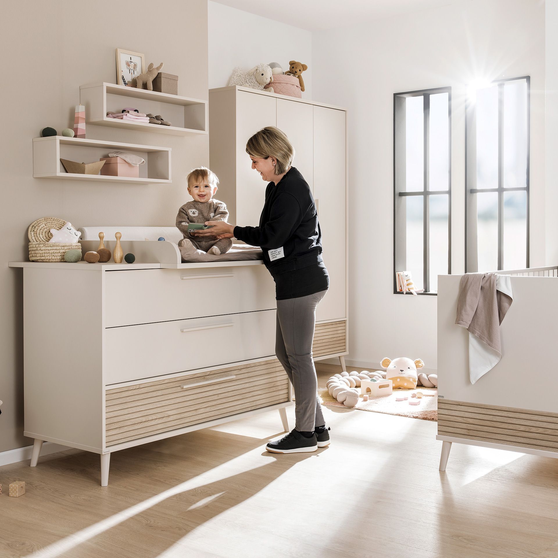 Eine Frau, die ein lächelndes Baby auf einem Wickeltisch in einem hellen, modernen Kinderzimmer wickelt.