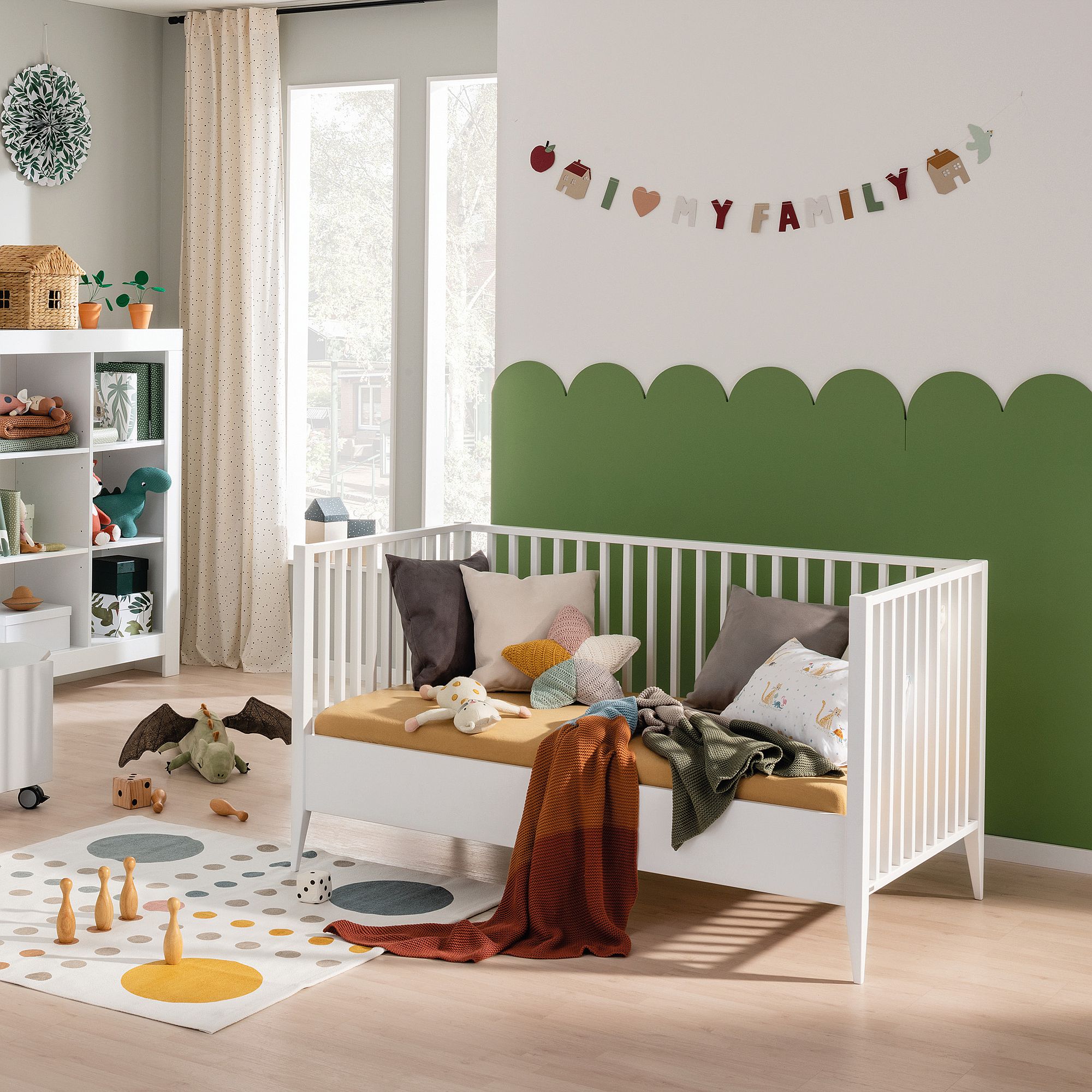 Ein gemütliches, modernes Kinderzimmer mit einem weißen Kinderbett, Spielzeug und einem My Family-Banner an der Wand.