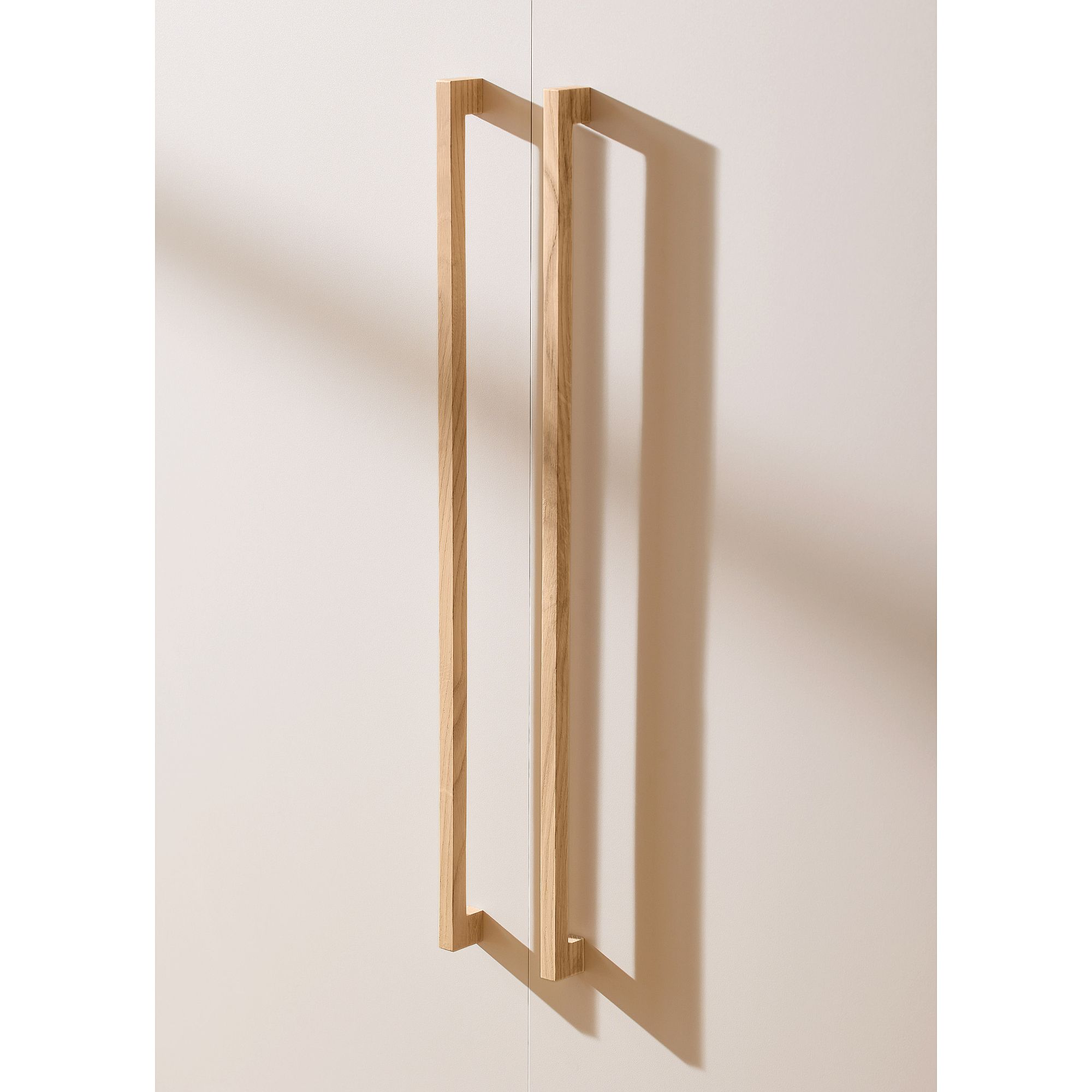 Minimalistische Holzgriffe an einer hellen Schranktür, die einen Schatten werfen.
