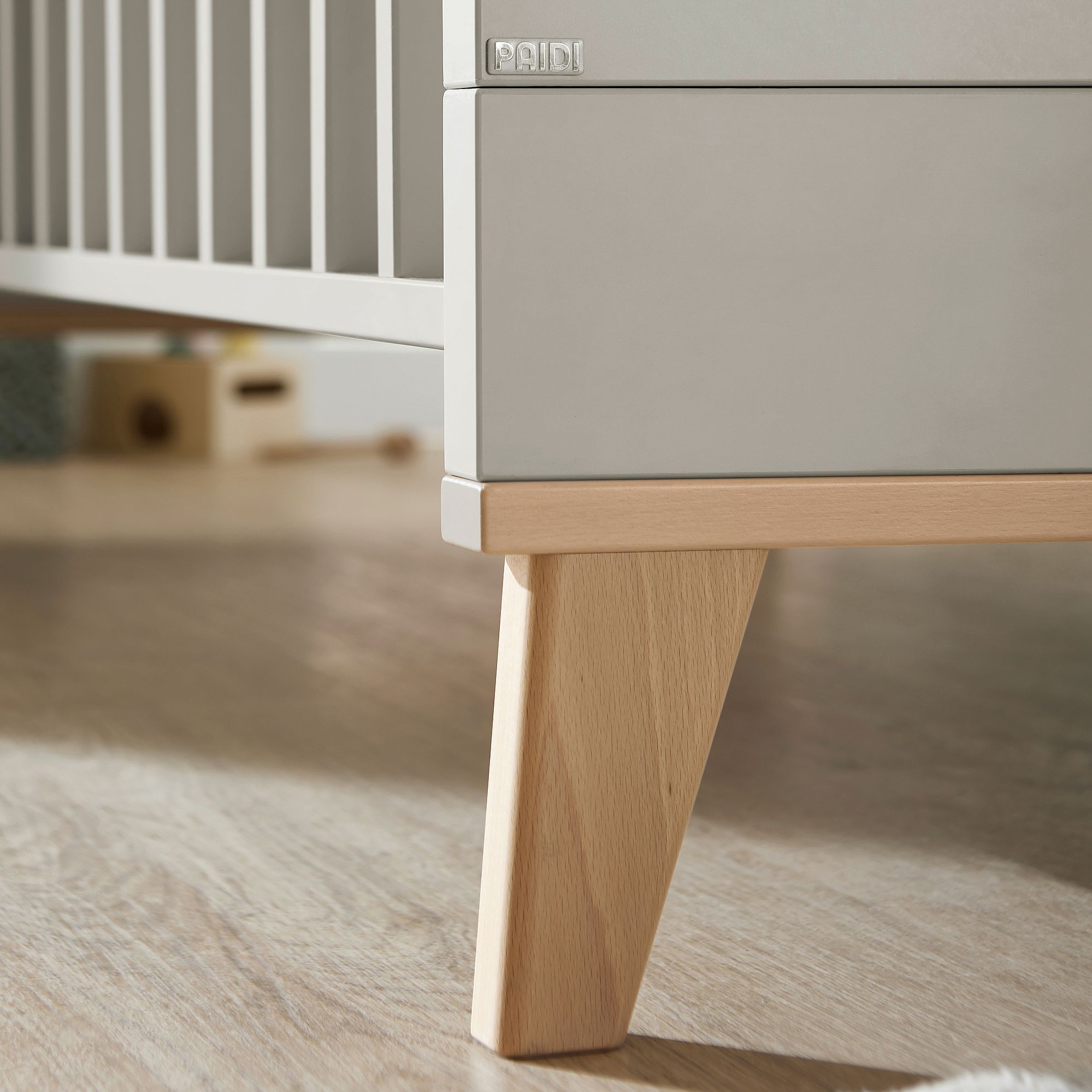 Close-up of a wooden crib leg on a light-colored floor.