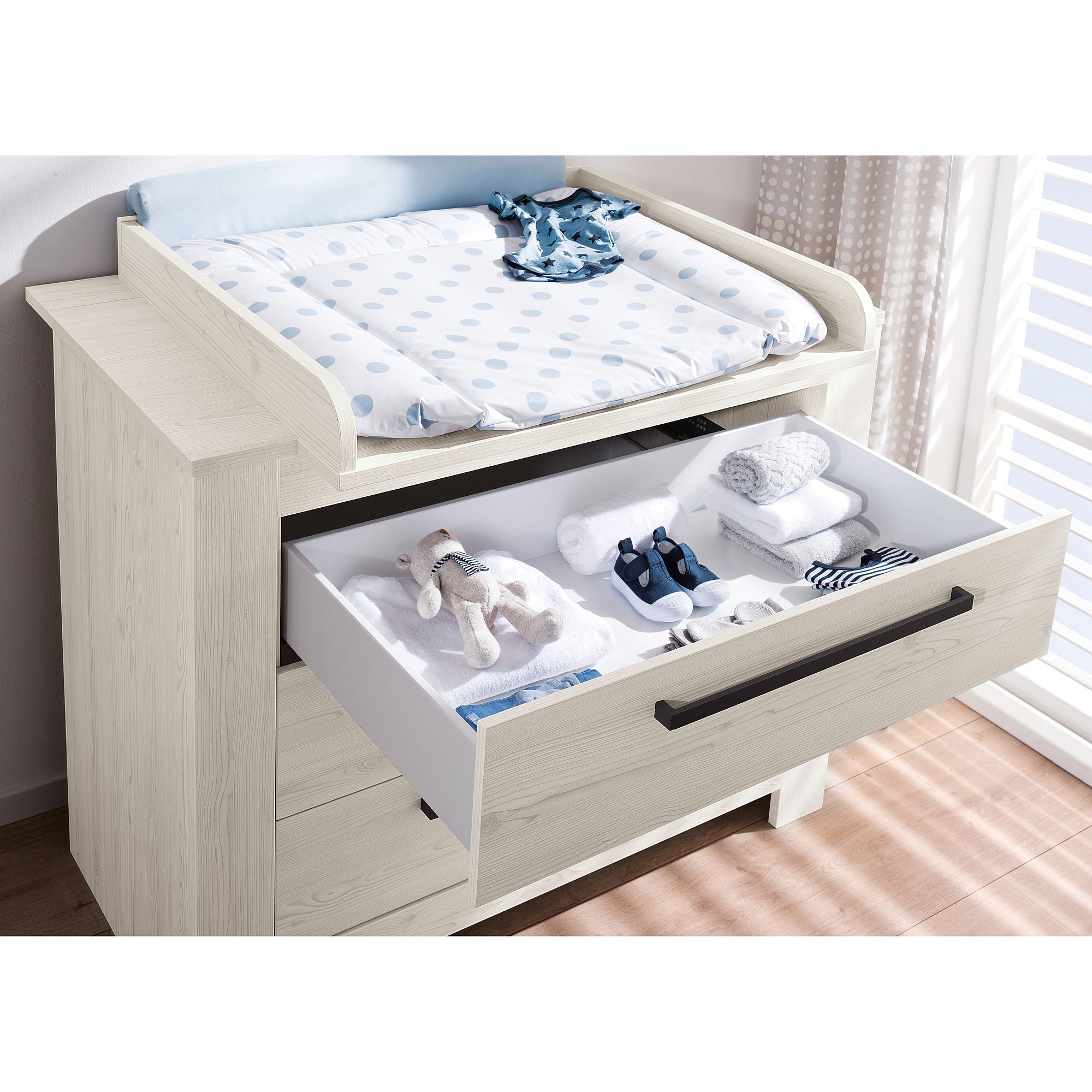 Weißer Wickeltisch mit offener Schublade für Babykleidung und Zubehör.