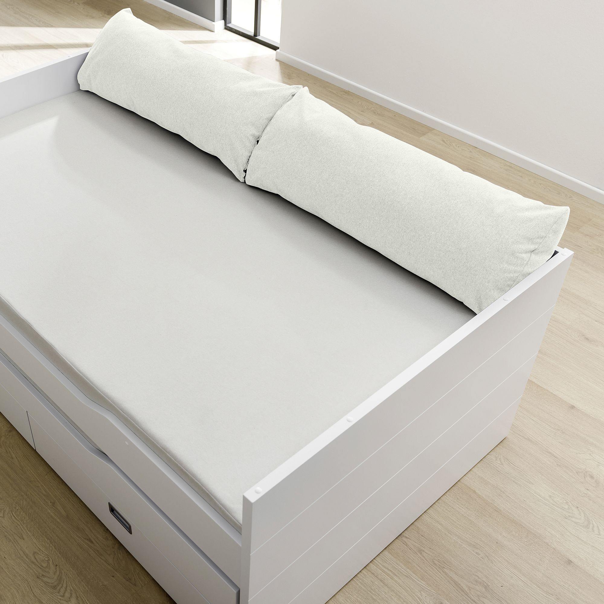 White daybed with storage drawers, topped with a long white pillow and sheet.