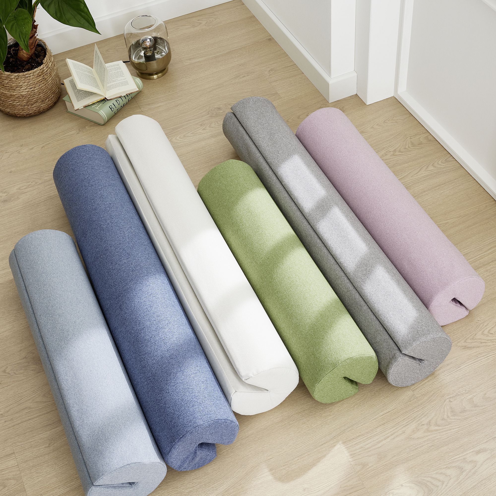 Six cylindrical bolsters in pastel colors laid out on a light wooden floor.