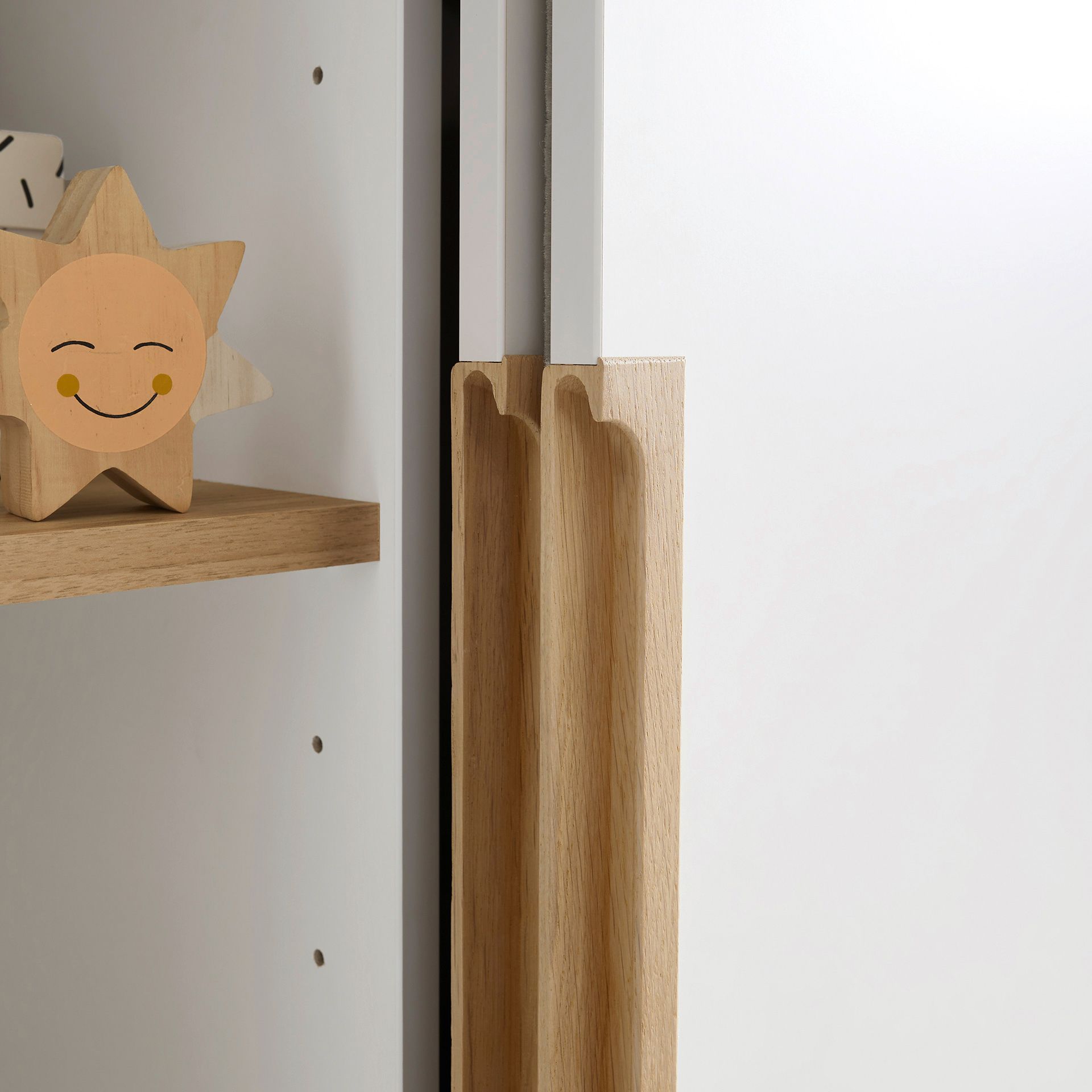 Schiebetürenschrank Yolanda mit 2 Schiebetüren und 2 Schubladen in 164 cm Nahaufnahme einer hölzernen Schrankkante mit einem lächelnden Sonnenspielzeug auf einem Regal.