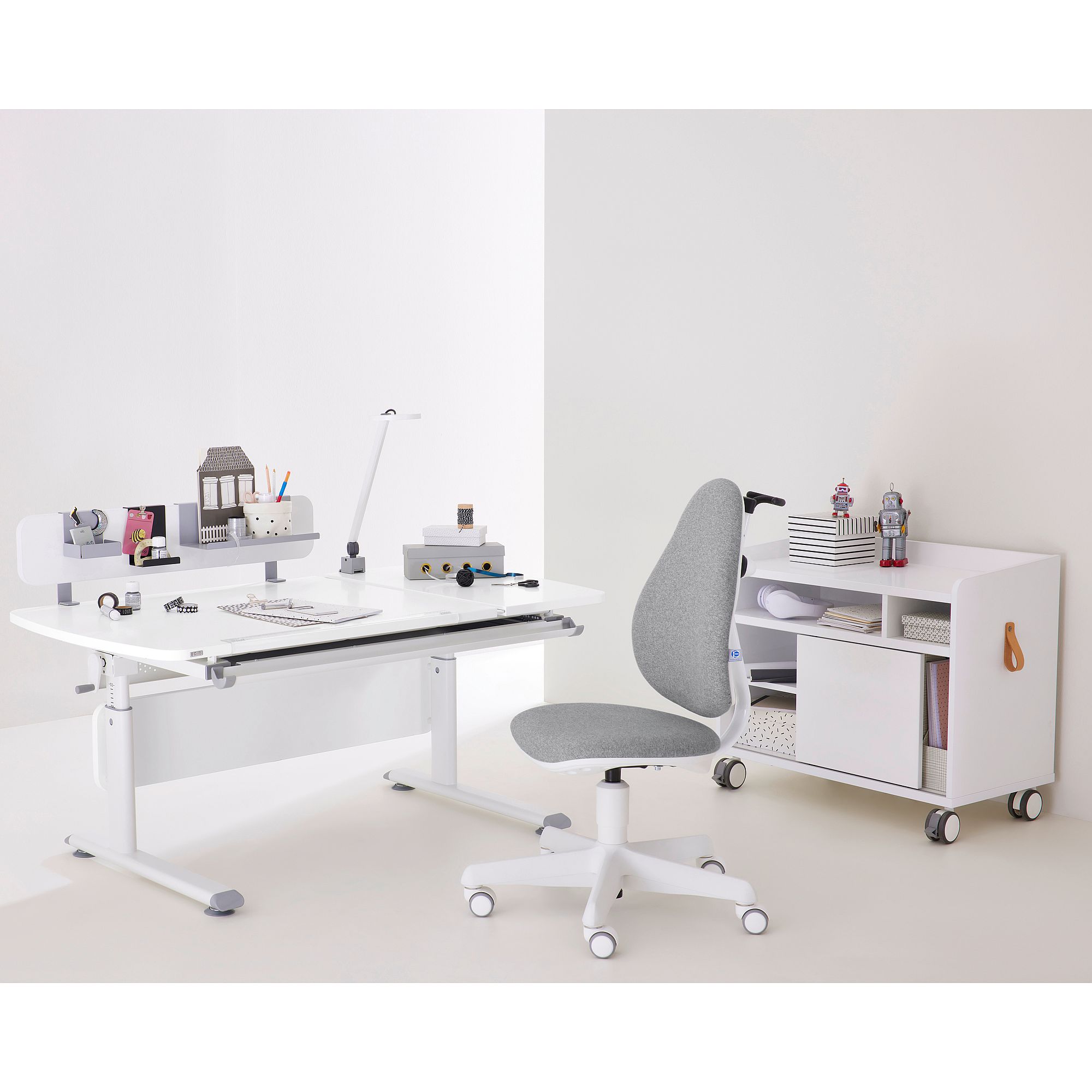 Minimalist white desk setup with grey chair, books, and small storage cabinet.