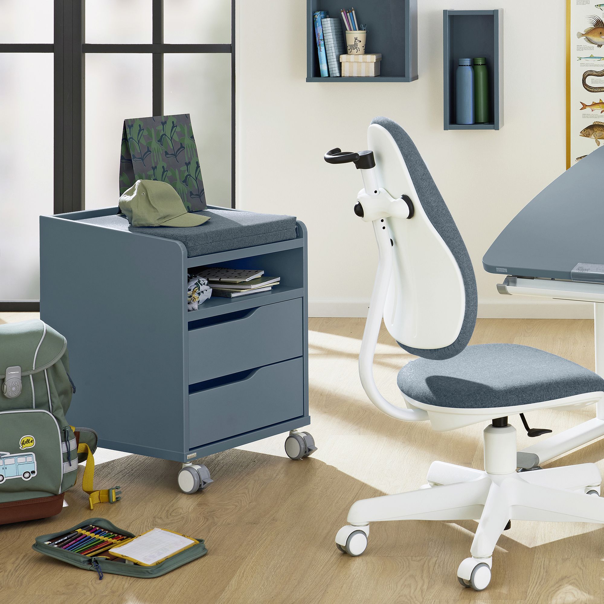 A modern blue rolling drawer unit and white chair in a bright study room.