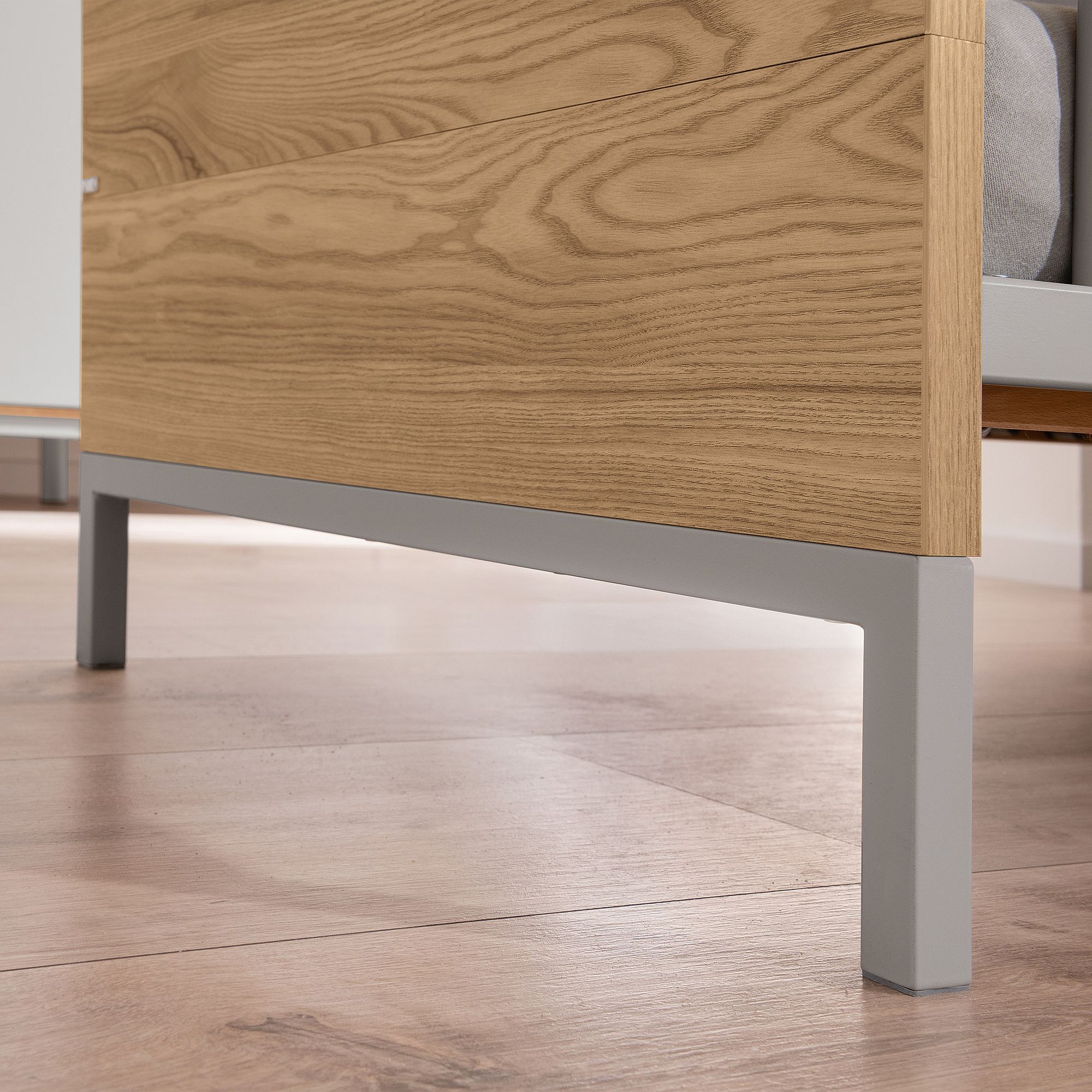 Nahaufnahme eines Bettgestells aus Holz mit grauen Metallbeinen auf einem Holzboden.