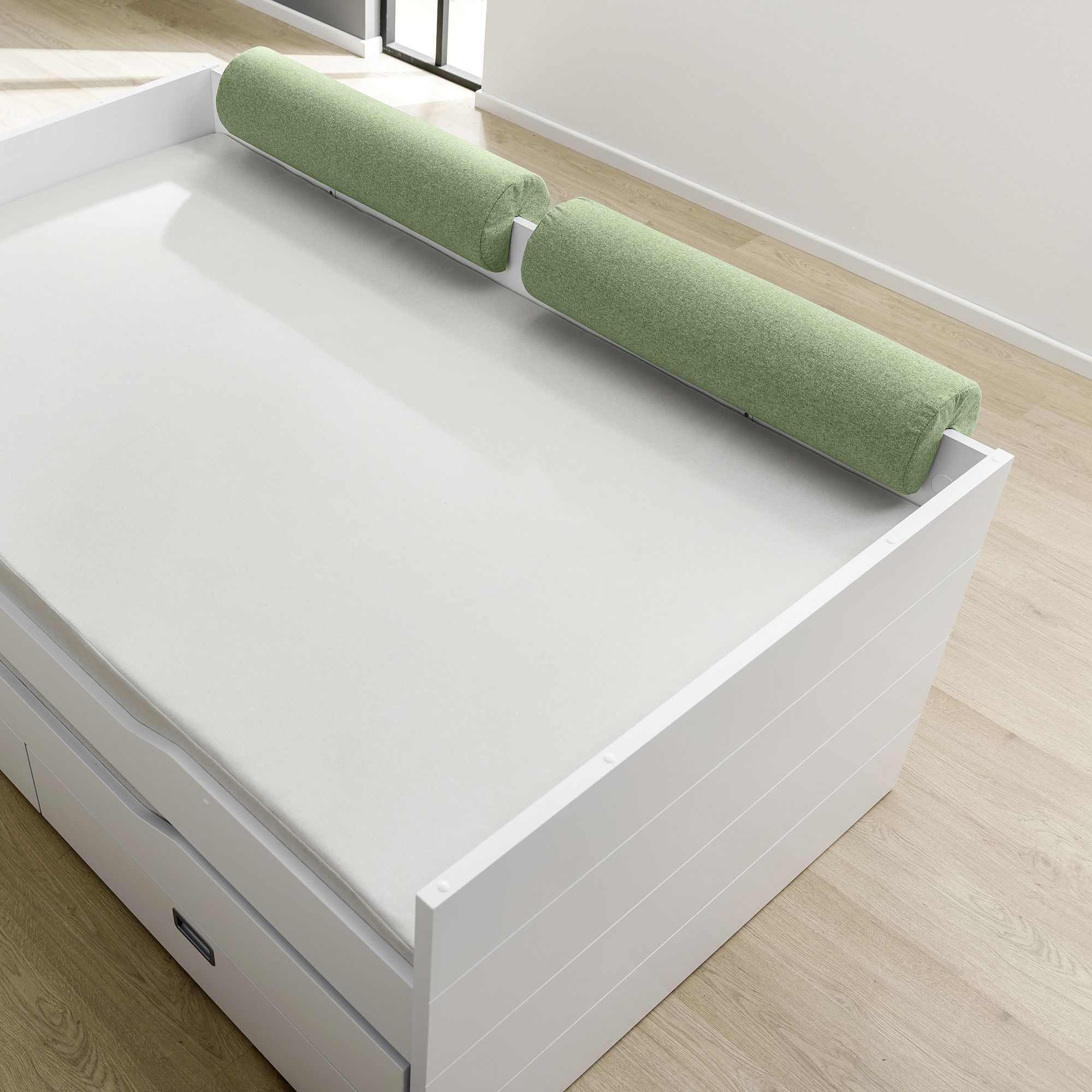 White daybed with green cylindrical cushions on a light wood floor.