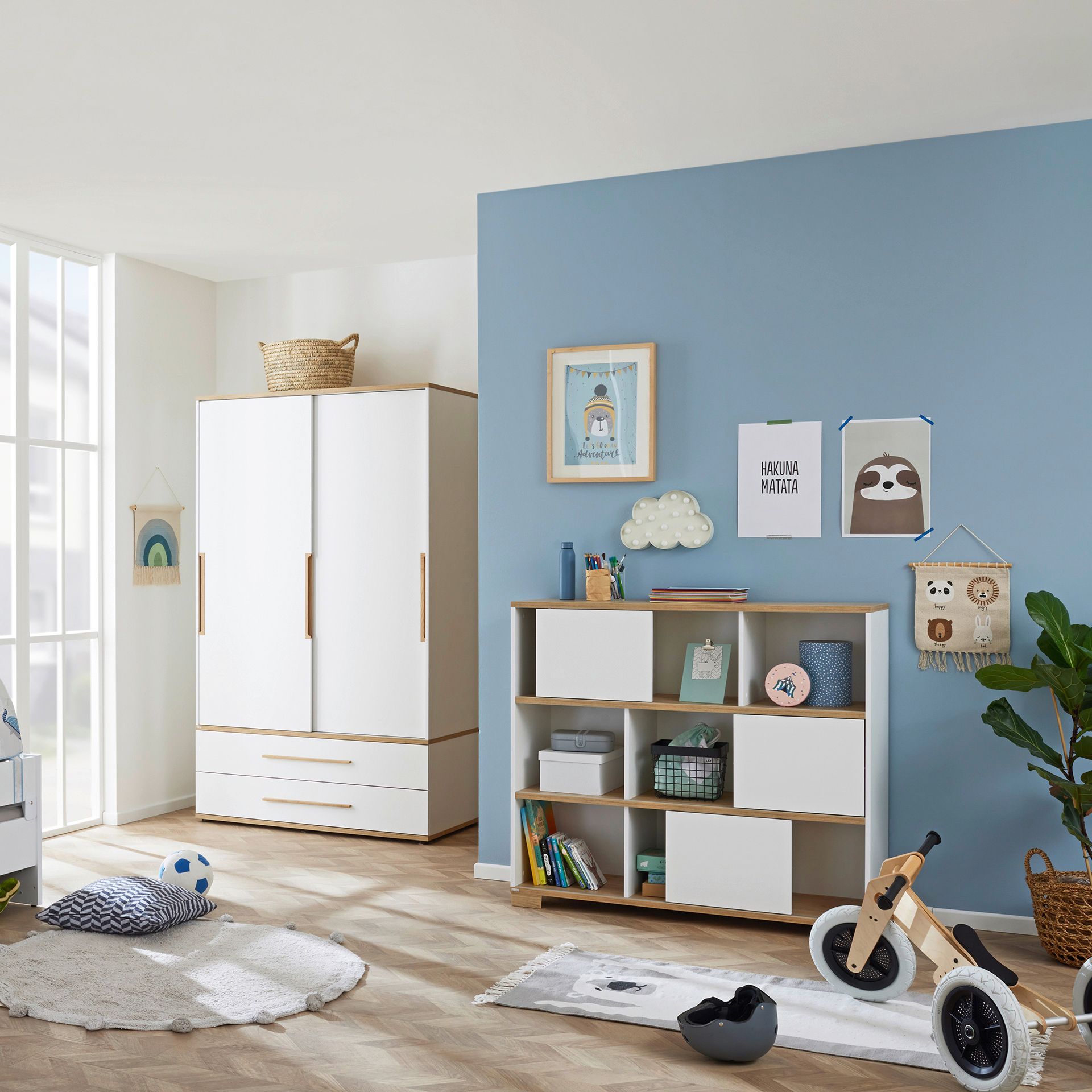 Modern nursery with white furniture, blue accent wall, and playful decor items.