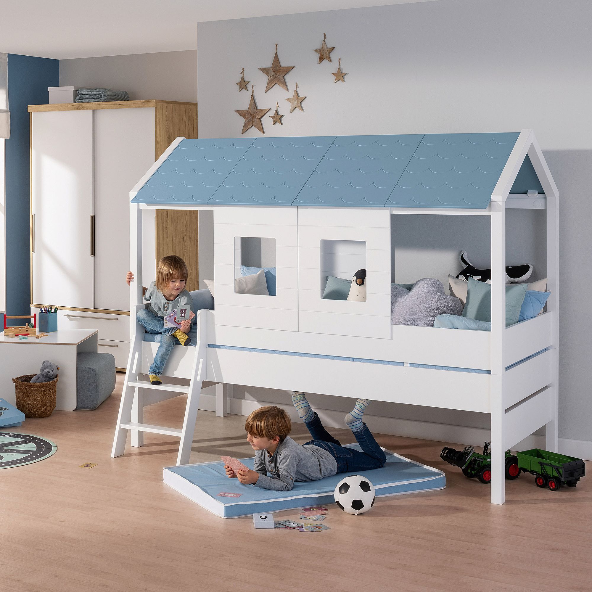 Zwei Kinder spielen in einem gemütlich eingerichteten Schlafzimmer neben einem hausförmigen Etagenbett.