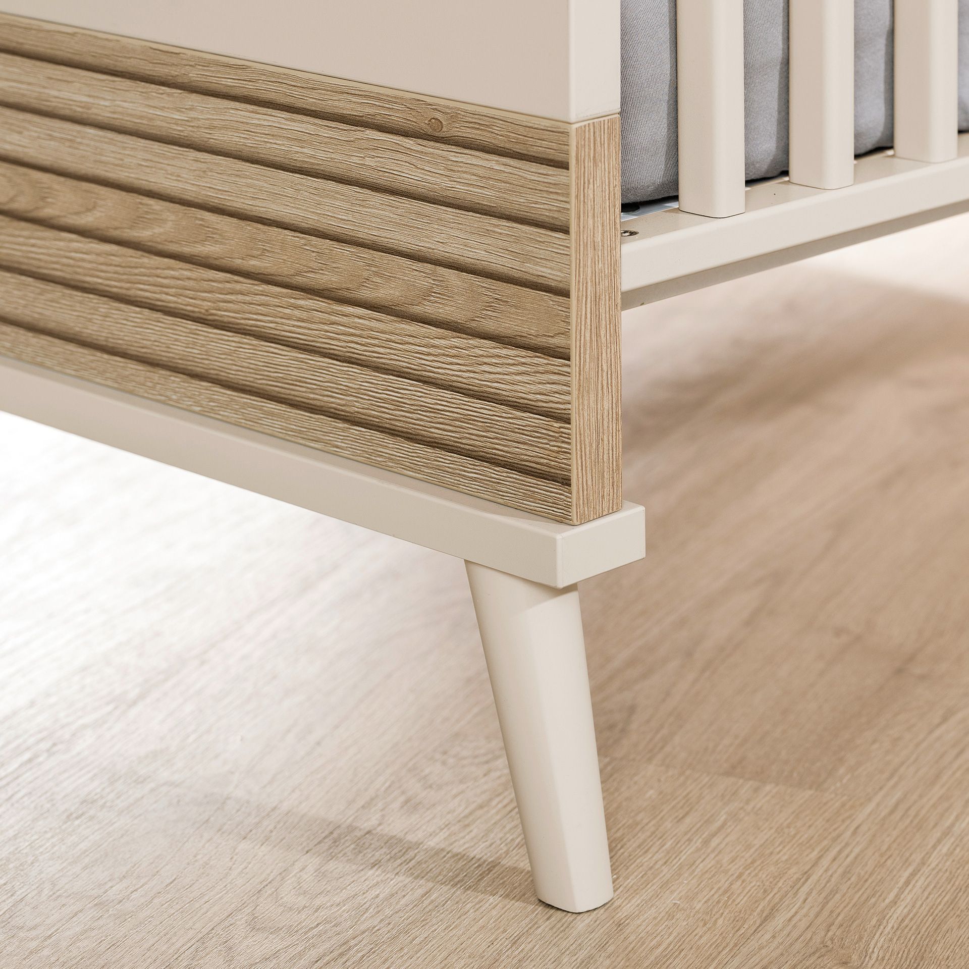 Nahaufnahme eines Krippenbeins mit Holzvertäfelung auf einem hellen Holzboden.