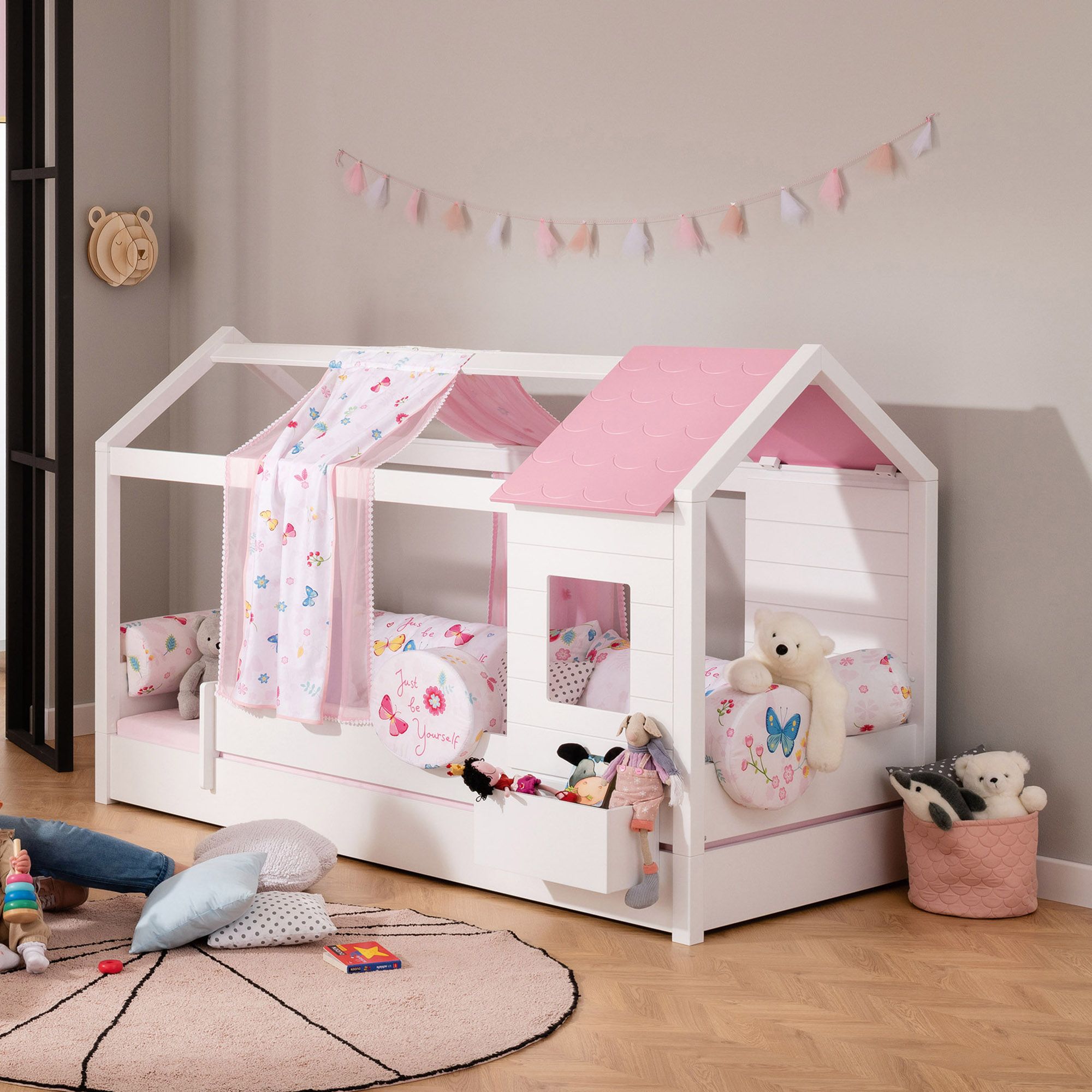 Weißes und rosafarbenes Kinderbett in Hausform mit Plüschtieren und verspieltem Dekor.