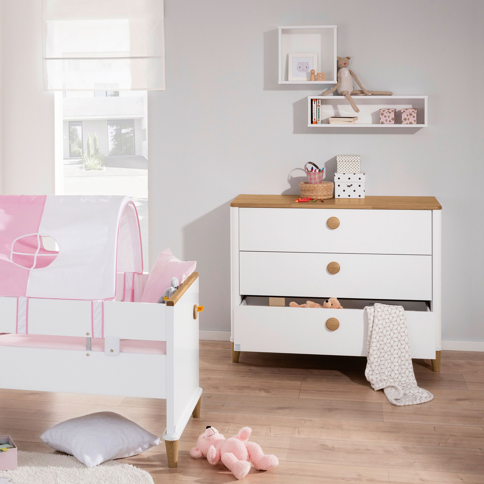 Wickelkommode Lotte & Fynn - Steiff by PAIDI 3 Schubladen A bright nursery with a bed, dresser, toys, and shelves on a wooden floor.