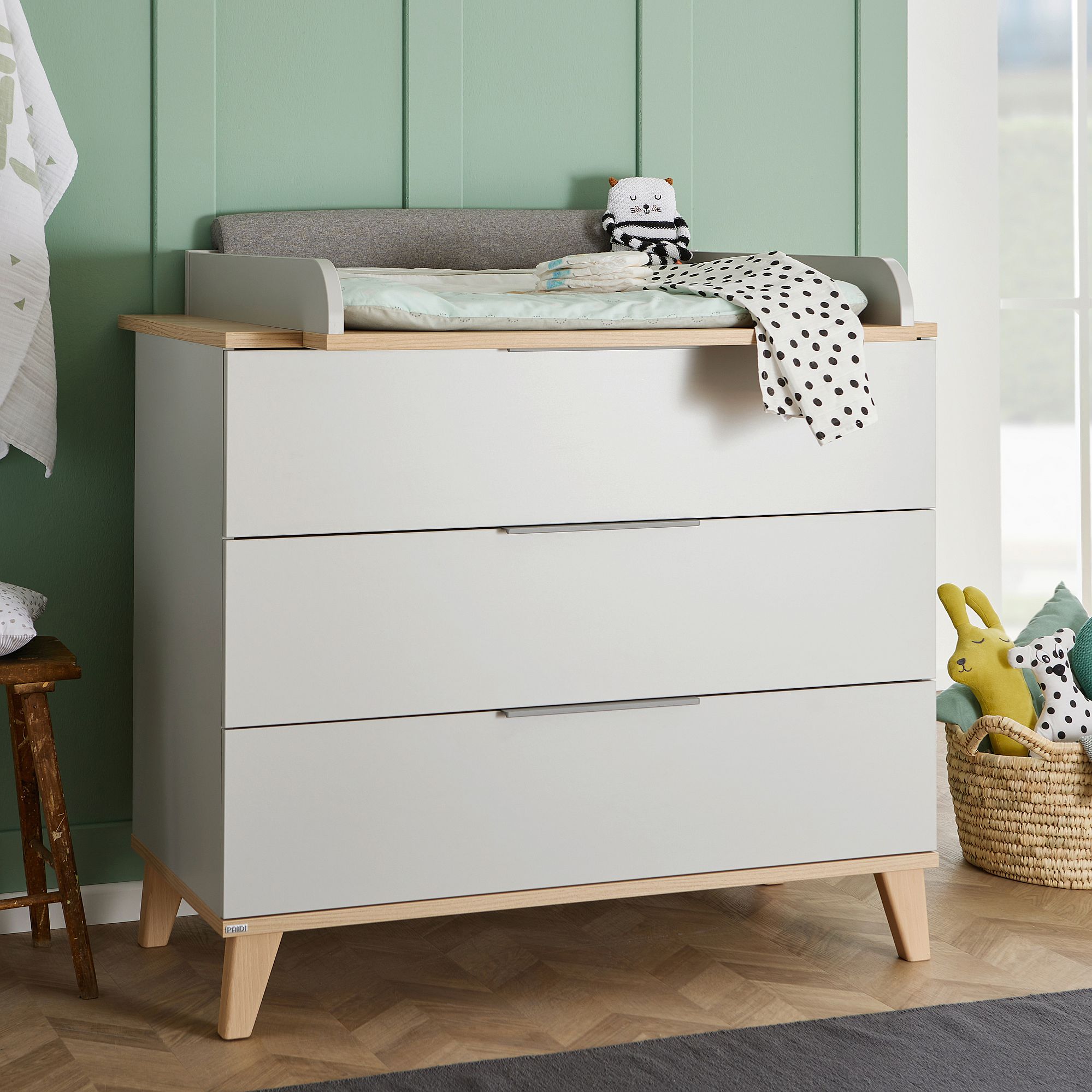 Wickelkommode Fiene mit 3 Schubladen Weiße Kommode mit Wickelauflage, Plüschtieren und einer gepunkteten Decke darauf.