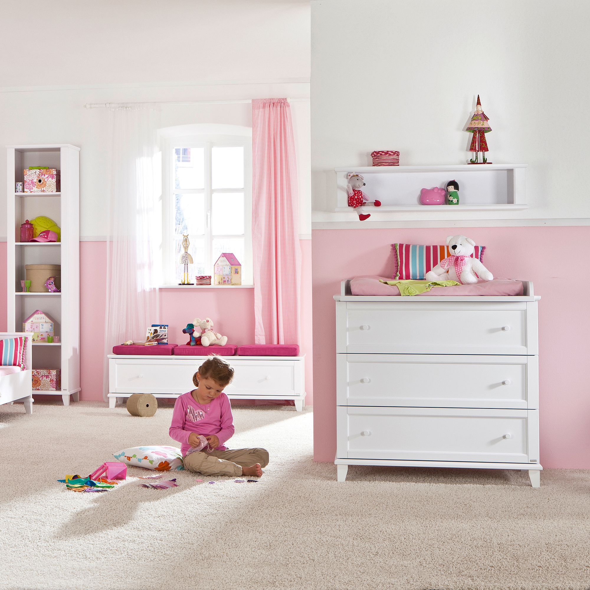 A young girl plays on the floor in a pink and white childrens bedroom.