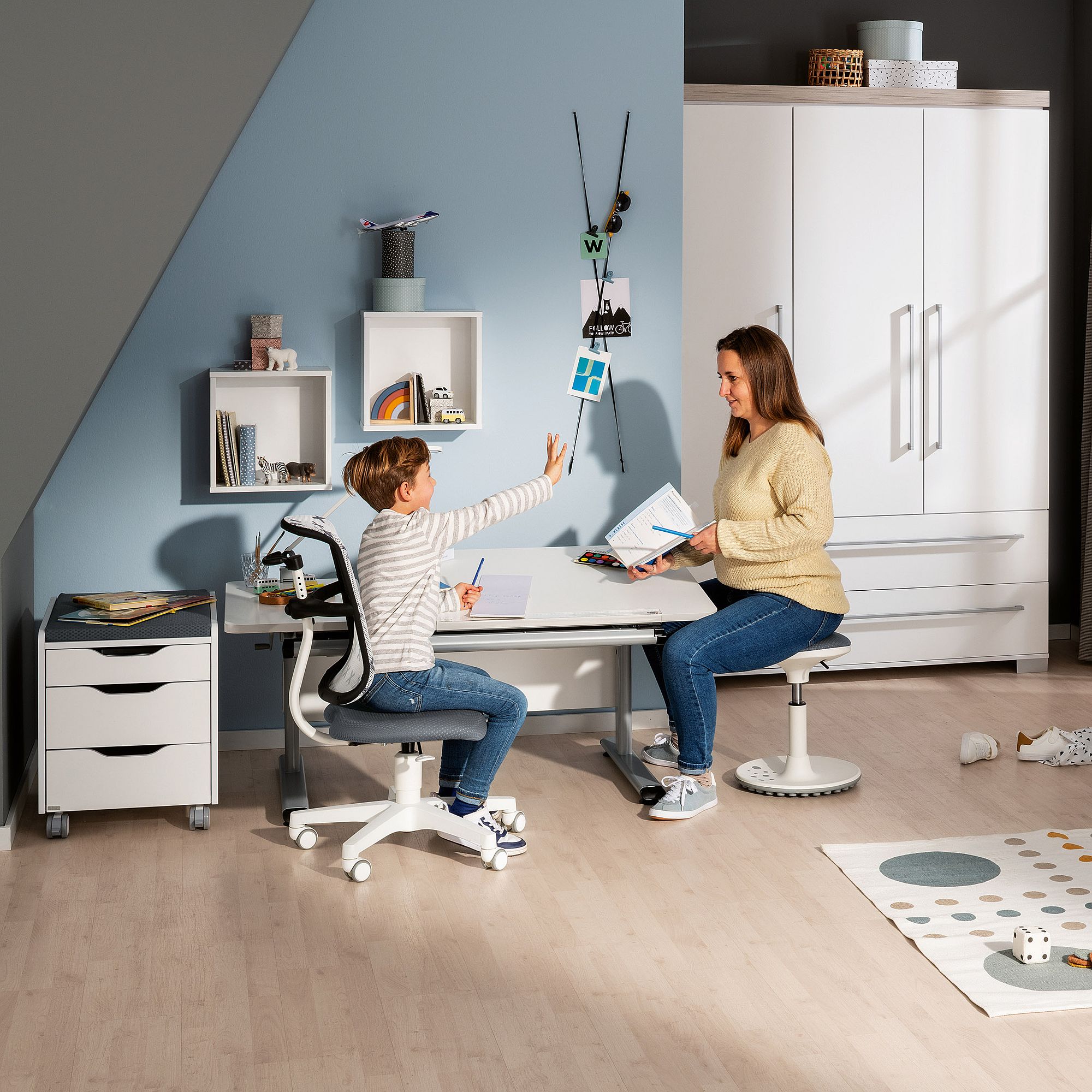 Eine Frau und ein Kind sitzen gemeinsam an einem Schreibtisch in einem modernen, hellen Heimbüro.